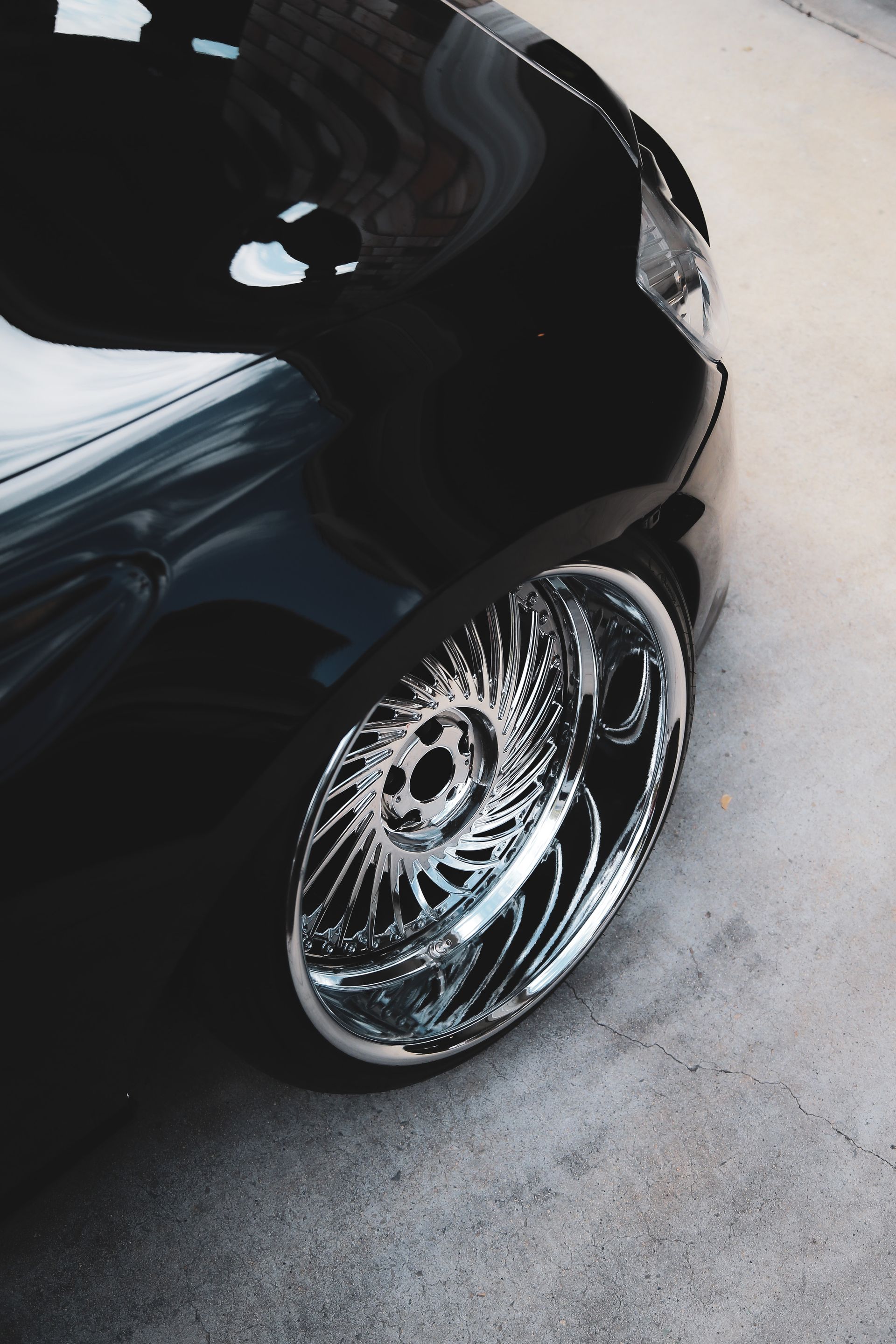 A close-up of a glossy black car fender and a shiny, intricate chrome custom wheel with a deep dish rim.