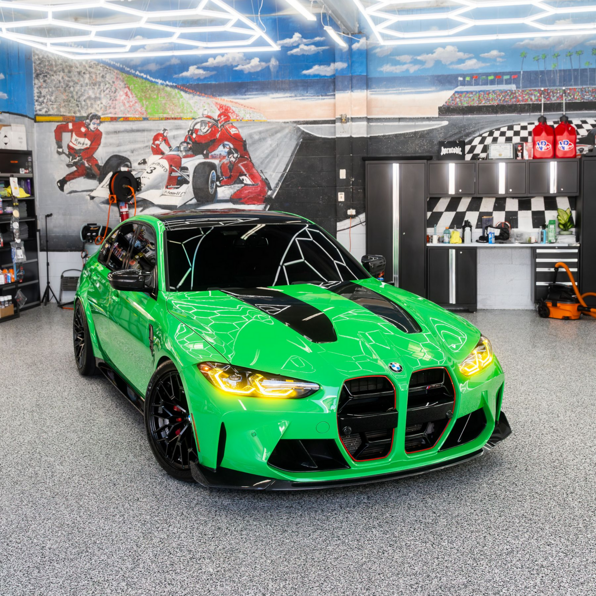 Bright green sports car with black stripes in a showroom, with motorcycles on the wall and checkered decor