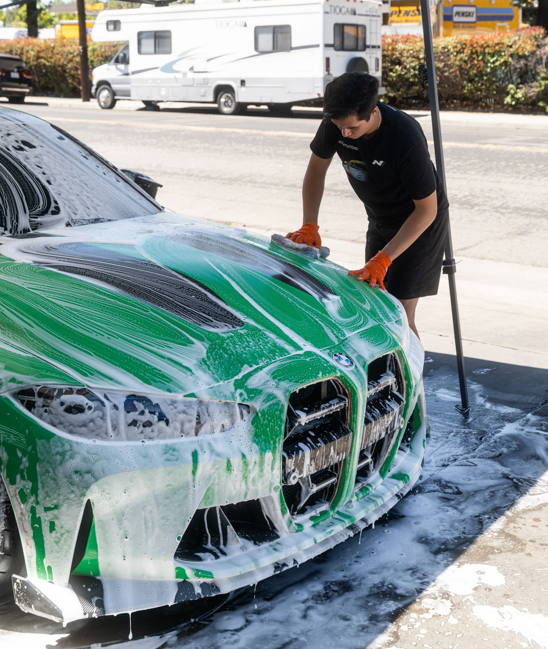 Person washing a green sports car with soap foam outdoors
