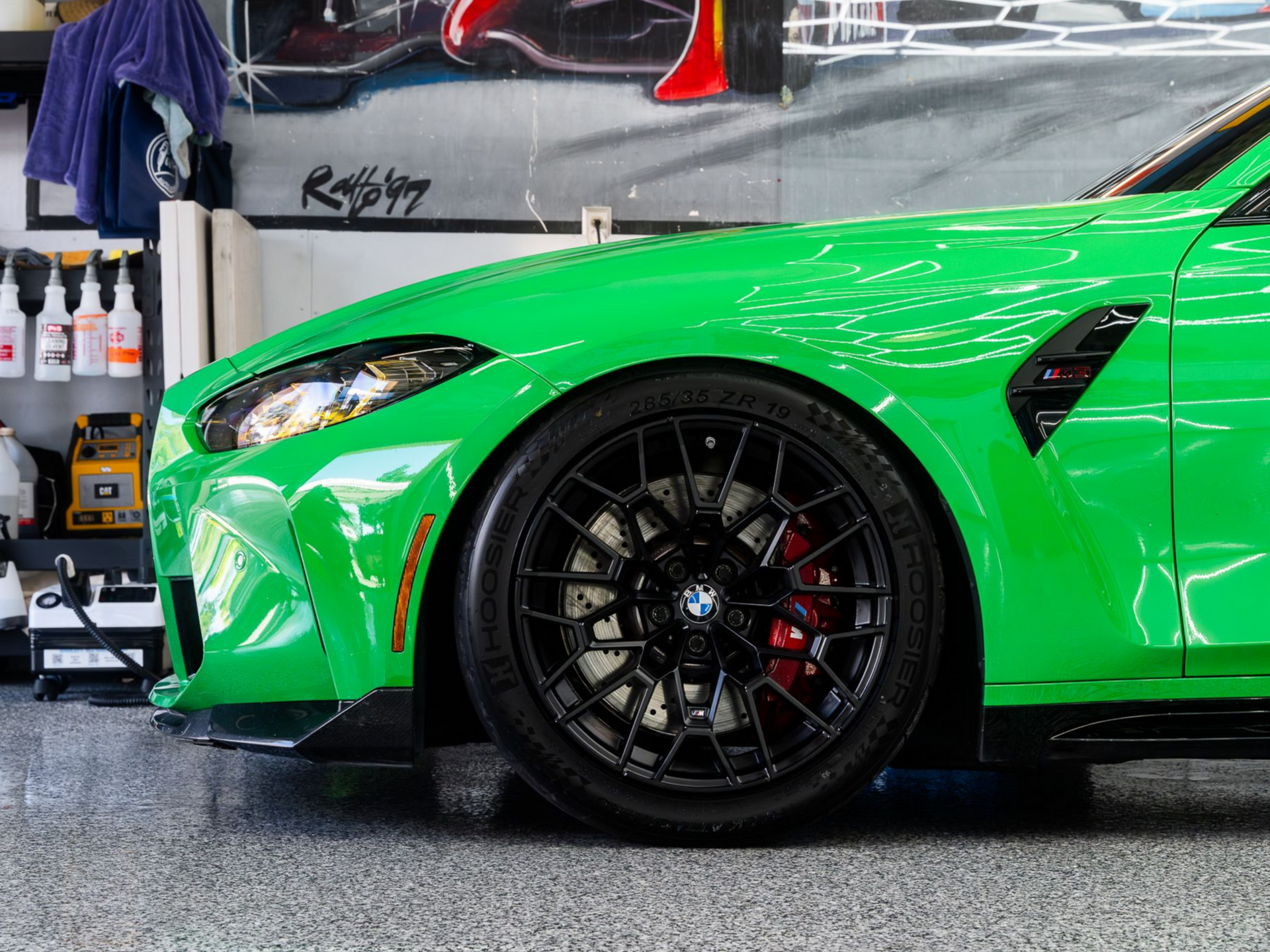A side view of a bright green BMW M3 parked in a garage, featuring black multi-spoke wheels and red brake calipers.