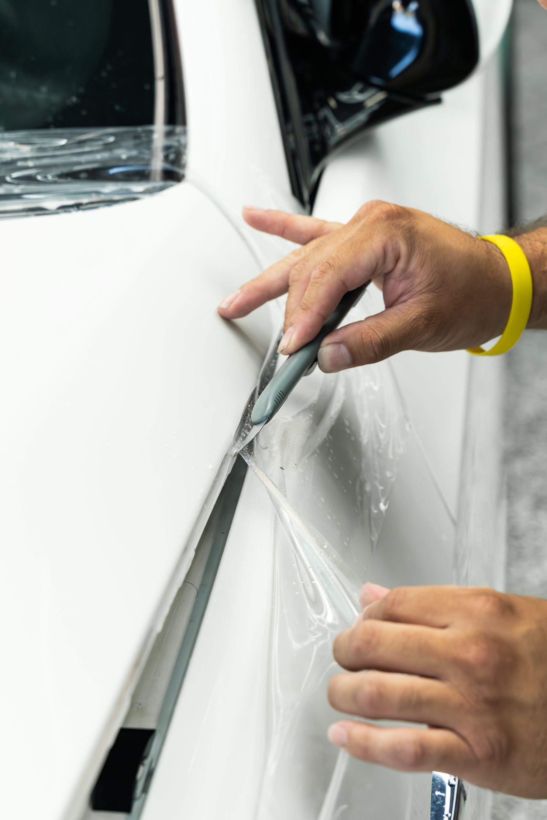 A technician uses a tool to trim protective film being applied to the white panel of a car.