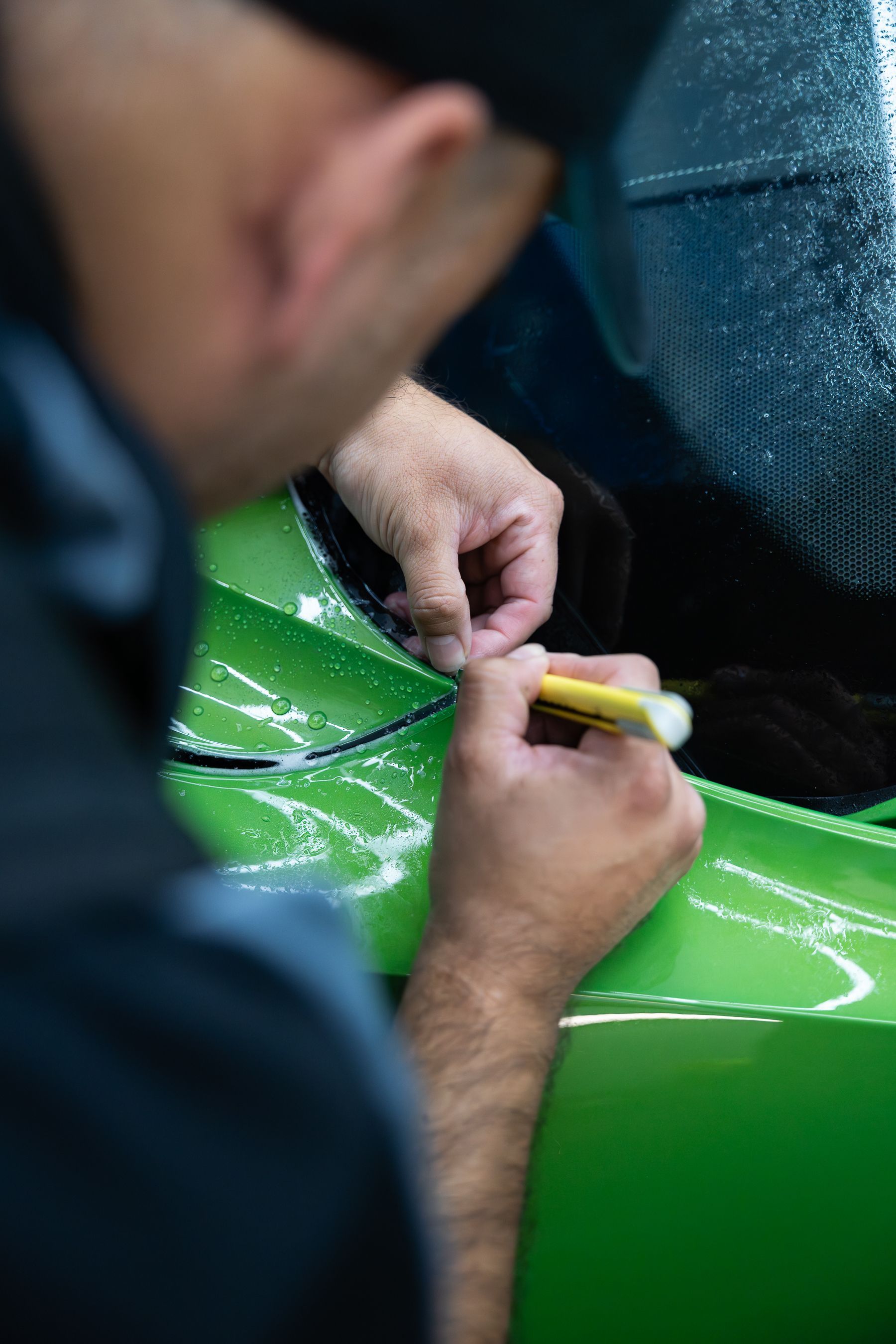 A person uses a yellow marker to trace a line on the bright green body panel of a vehicle.