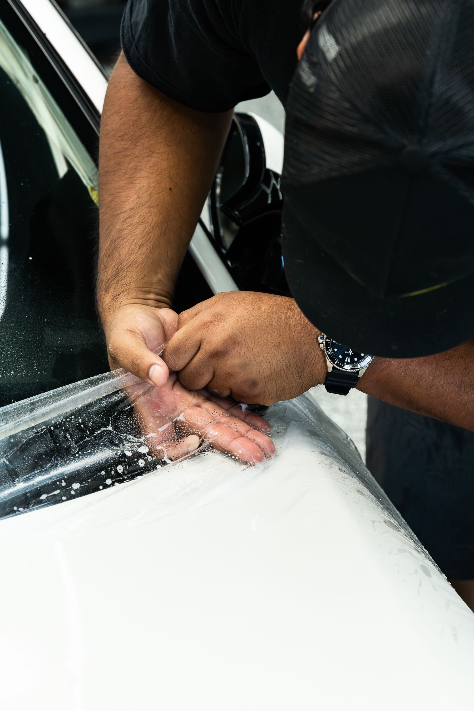 A person applying a clear protective film onto the hood of a white vehicle.