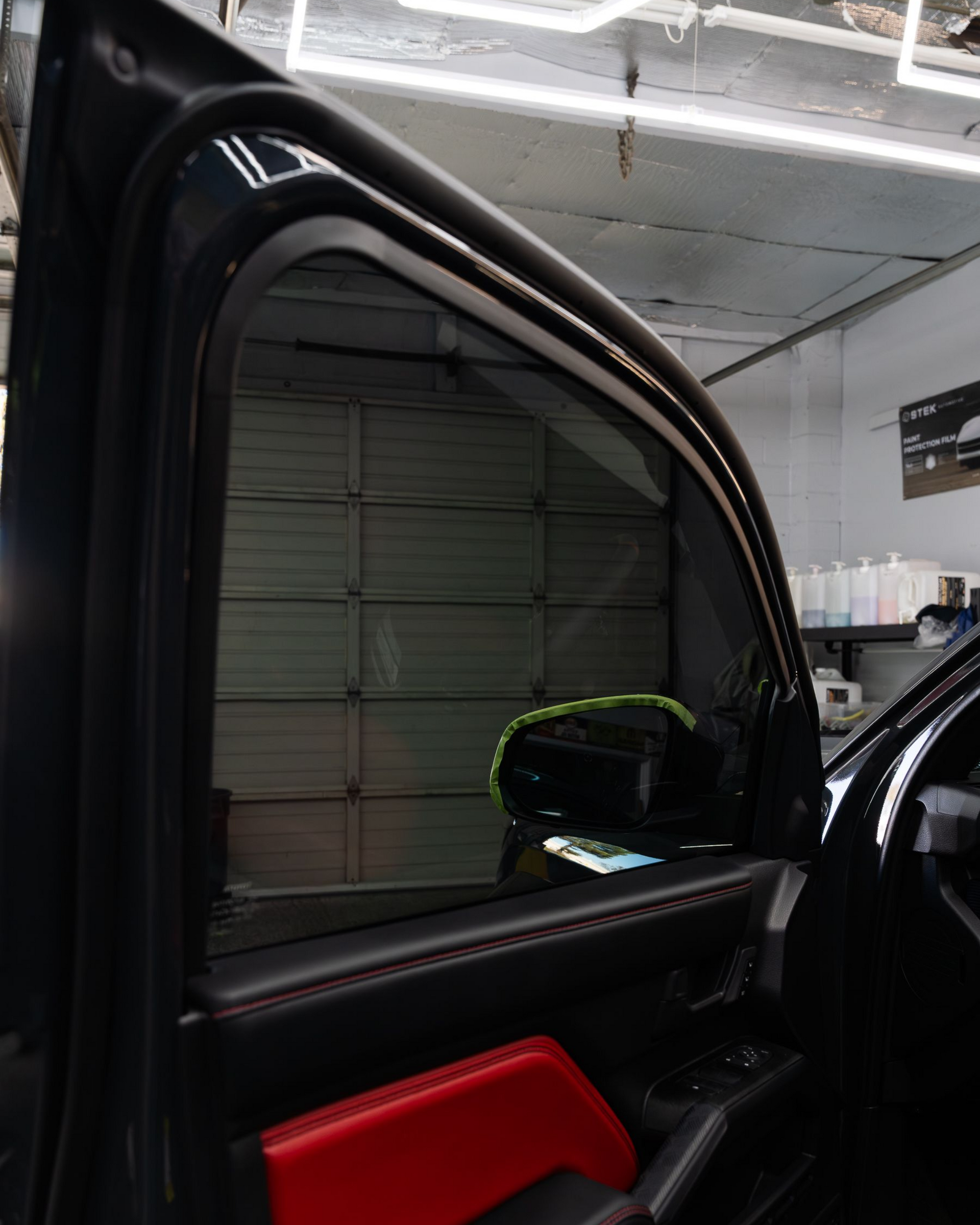 The interior of a car door, featuring a tinted window and red upholstery, inside a garage.