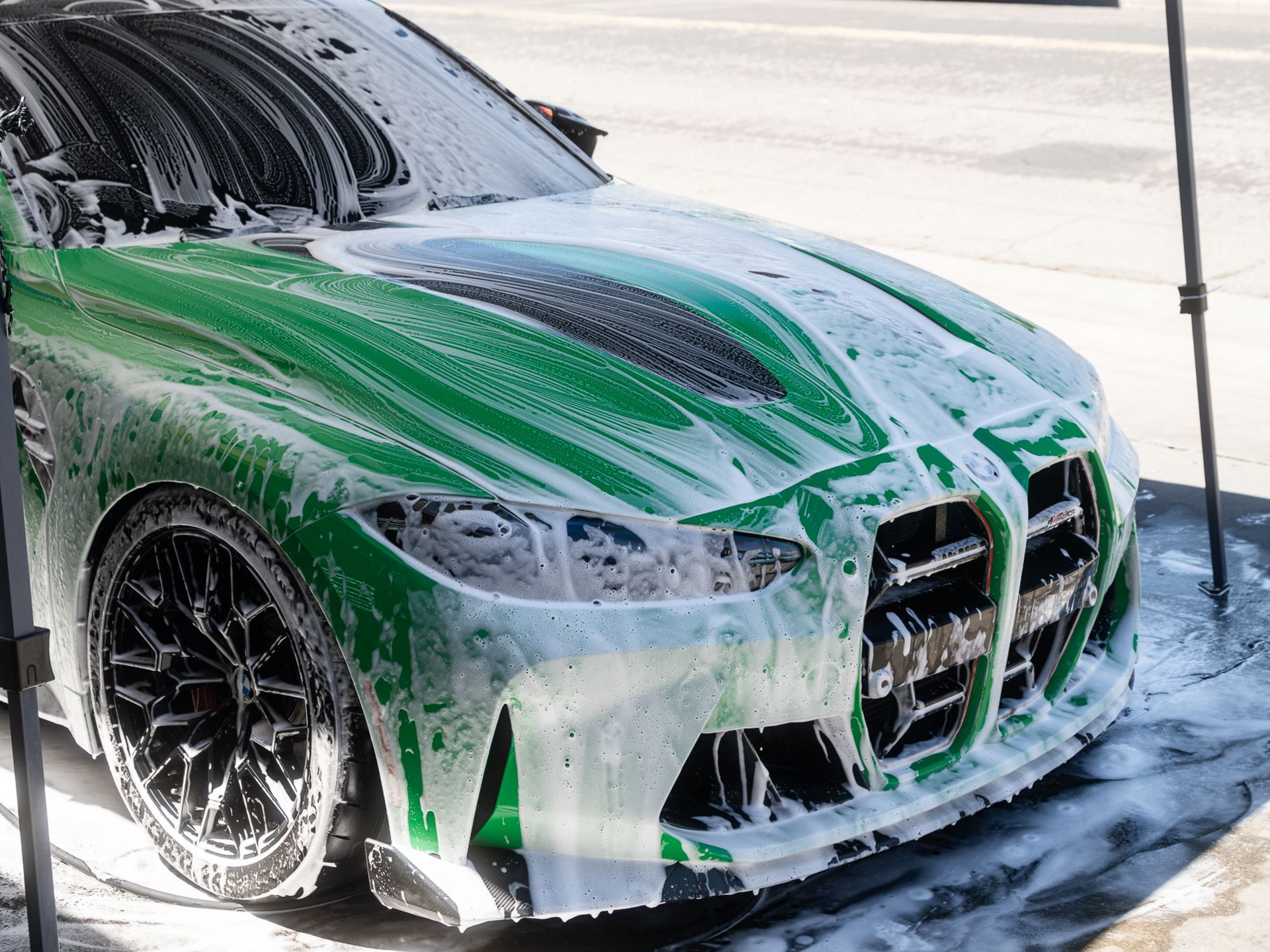 A vibrant green BMW sports car covered in thick white soap suds at a car wash.