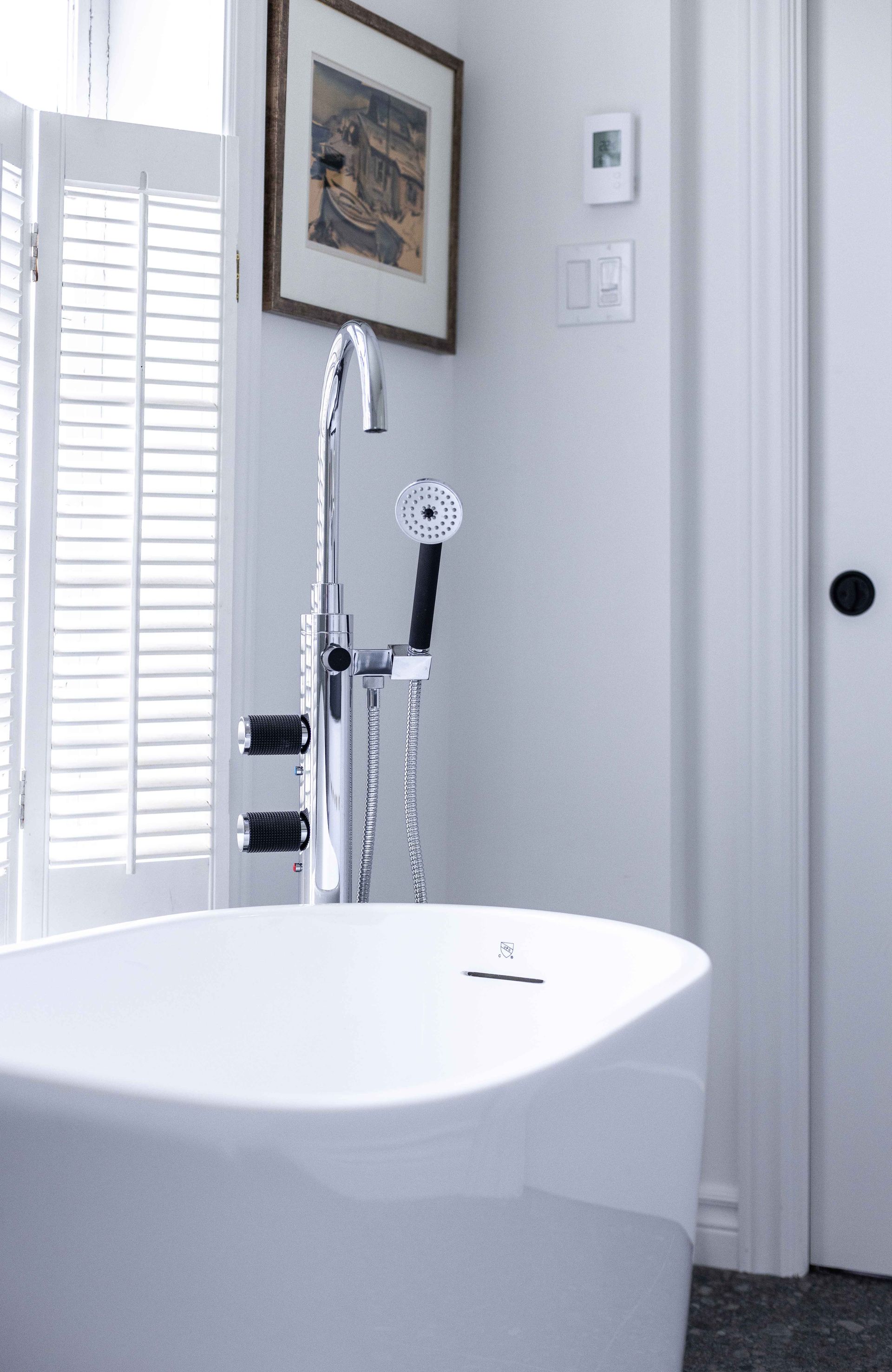 Baignoire blanche avec robinet chromé, à côté d'une fenêtre à volets.