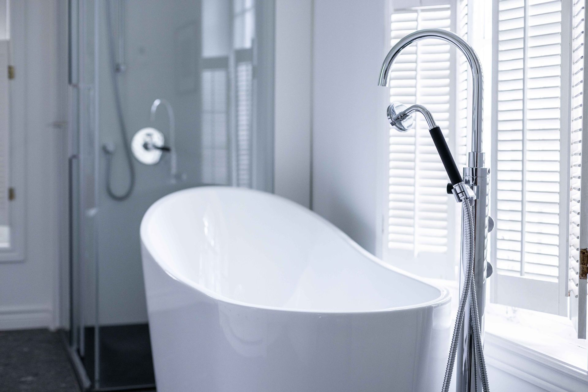 Baignoire îlot moderne blanche avec pommeau de douche et fenêtre à volets.