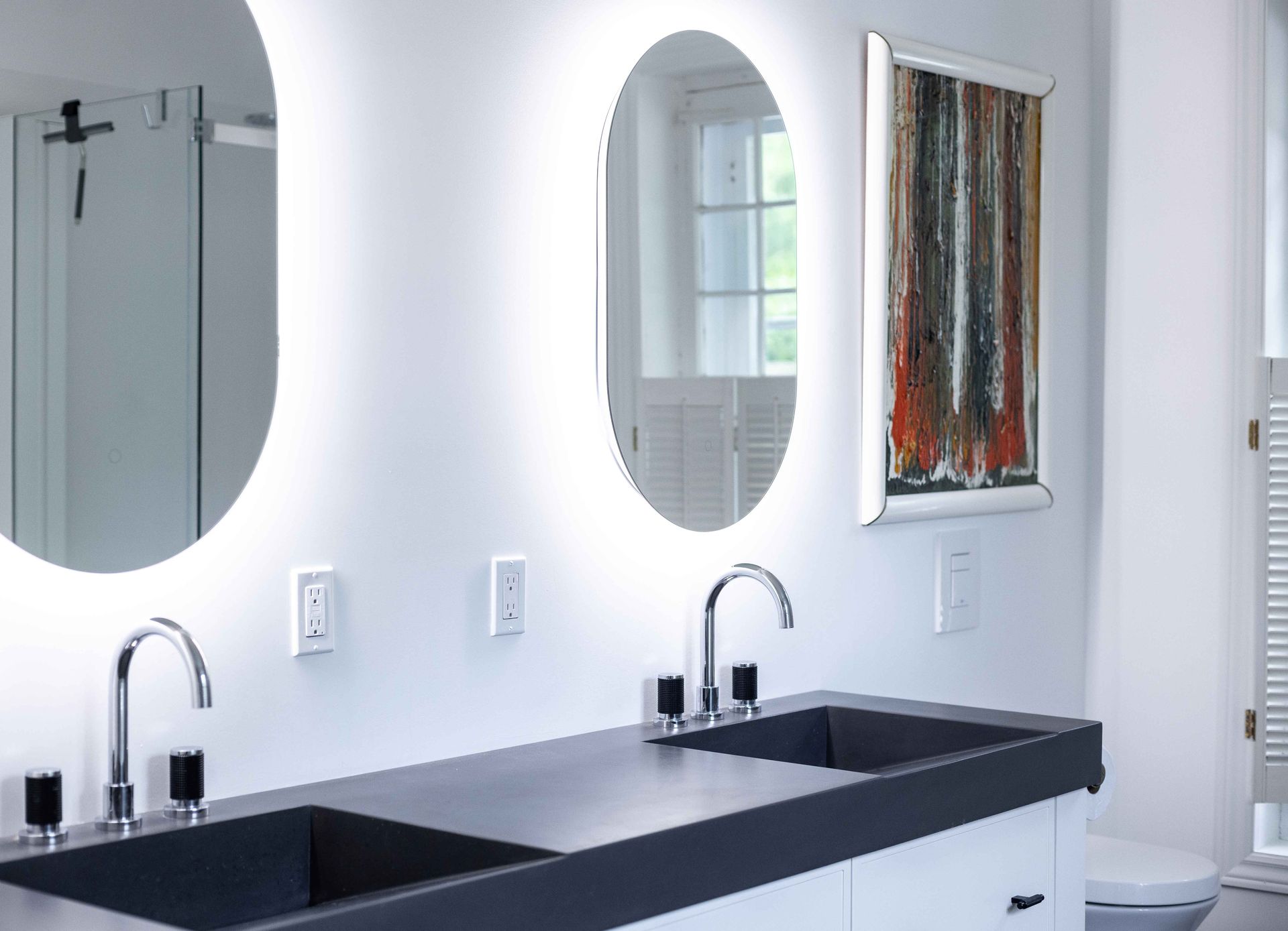 Salle de bains avec deux miroirs ovales rétroéclairés au-dessus d'un meuble-lavabo à double vasque orné d'une œuvre d'art.