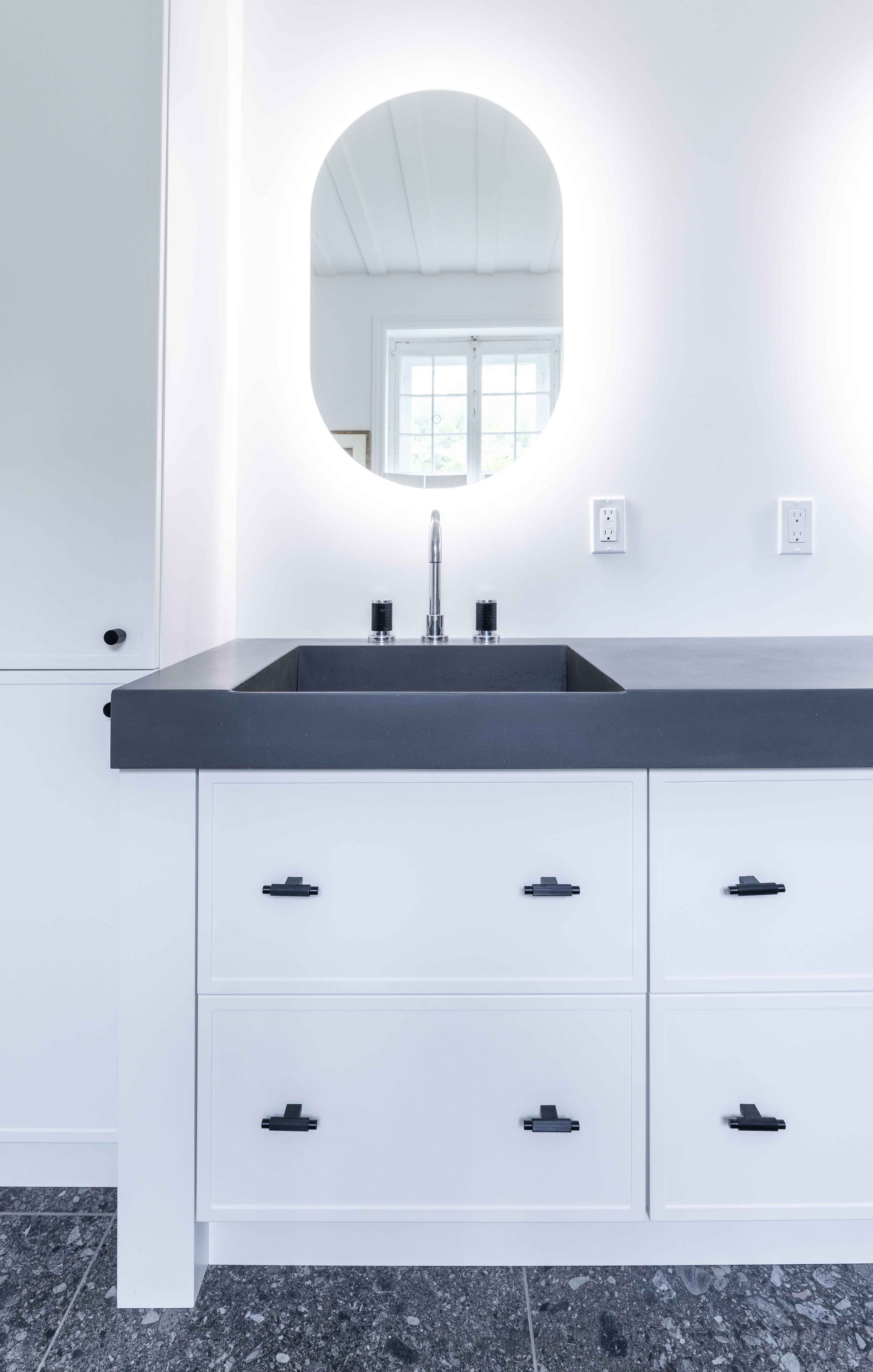 Meuble-lavabo blanc avec comptoir foncé, miroir ovale rétroéclairé et quincaillerie foncée.