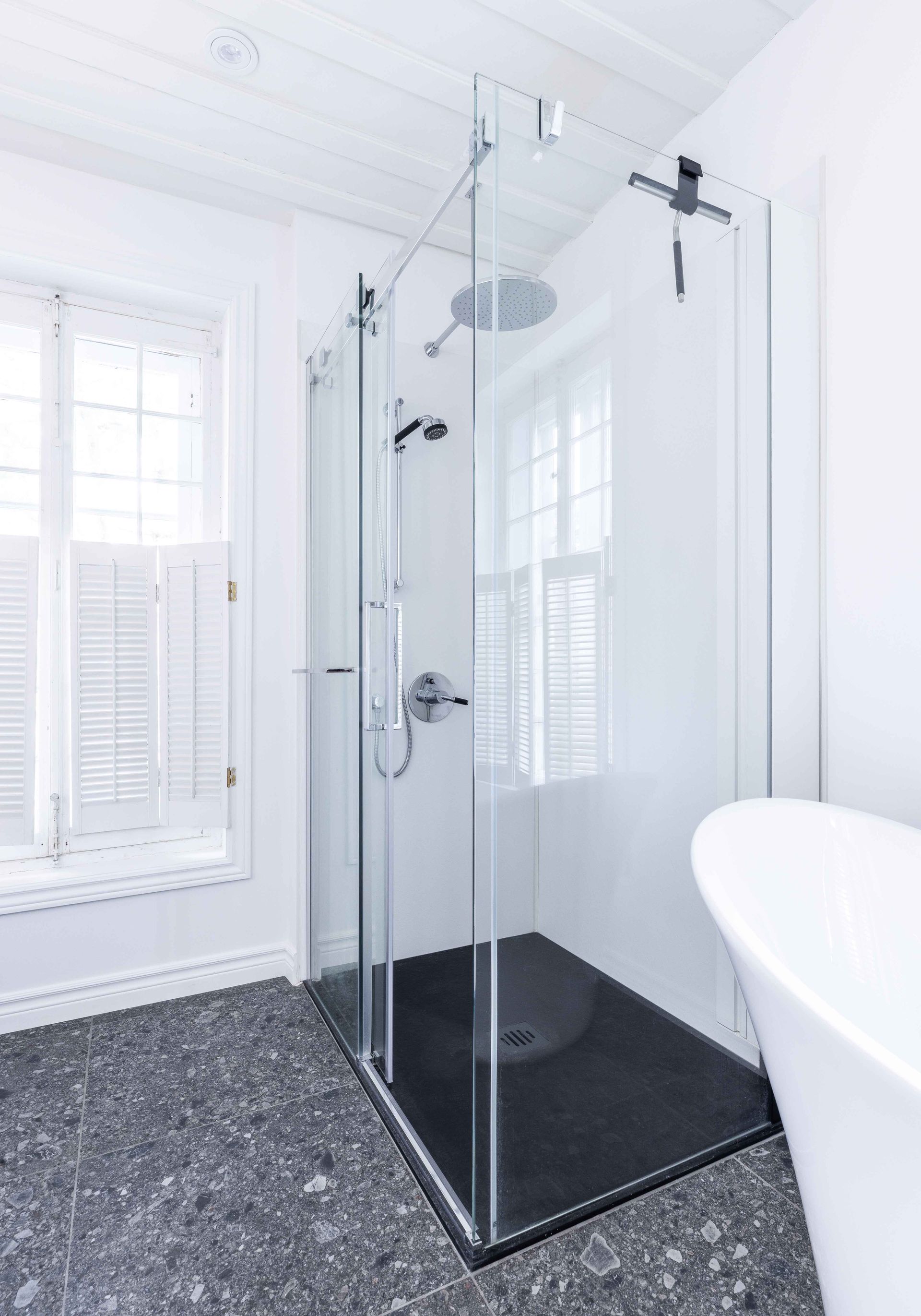 Cabine de douche en verre dans une salle de bains blanche avec sol carrelé gris foncé.