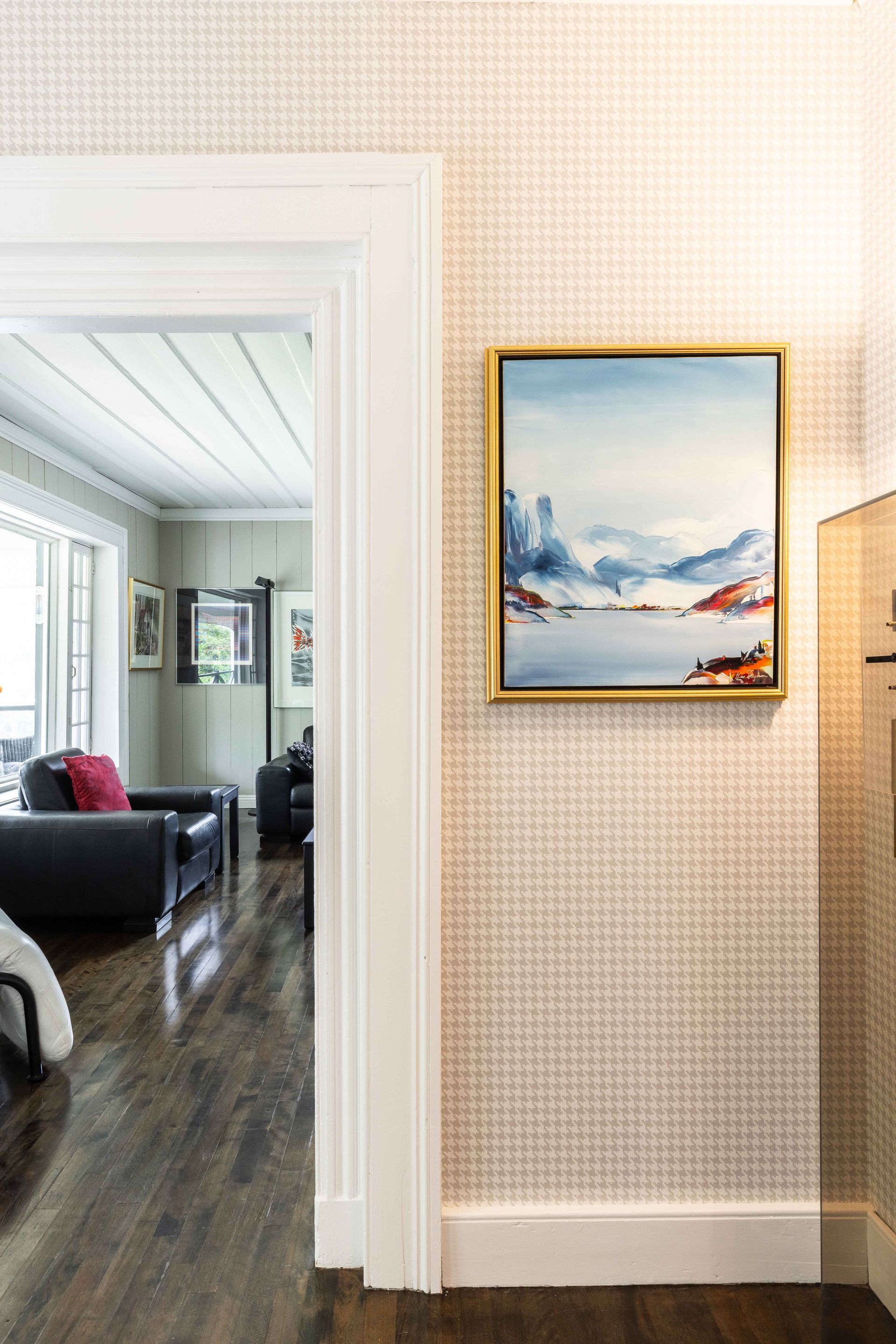 Couloir avec papier peint à motifs, œuvres d'art encadrées et aperçu d'un salon avec parquet foncé.
