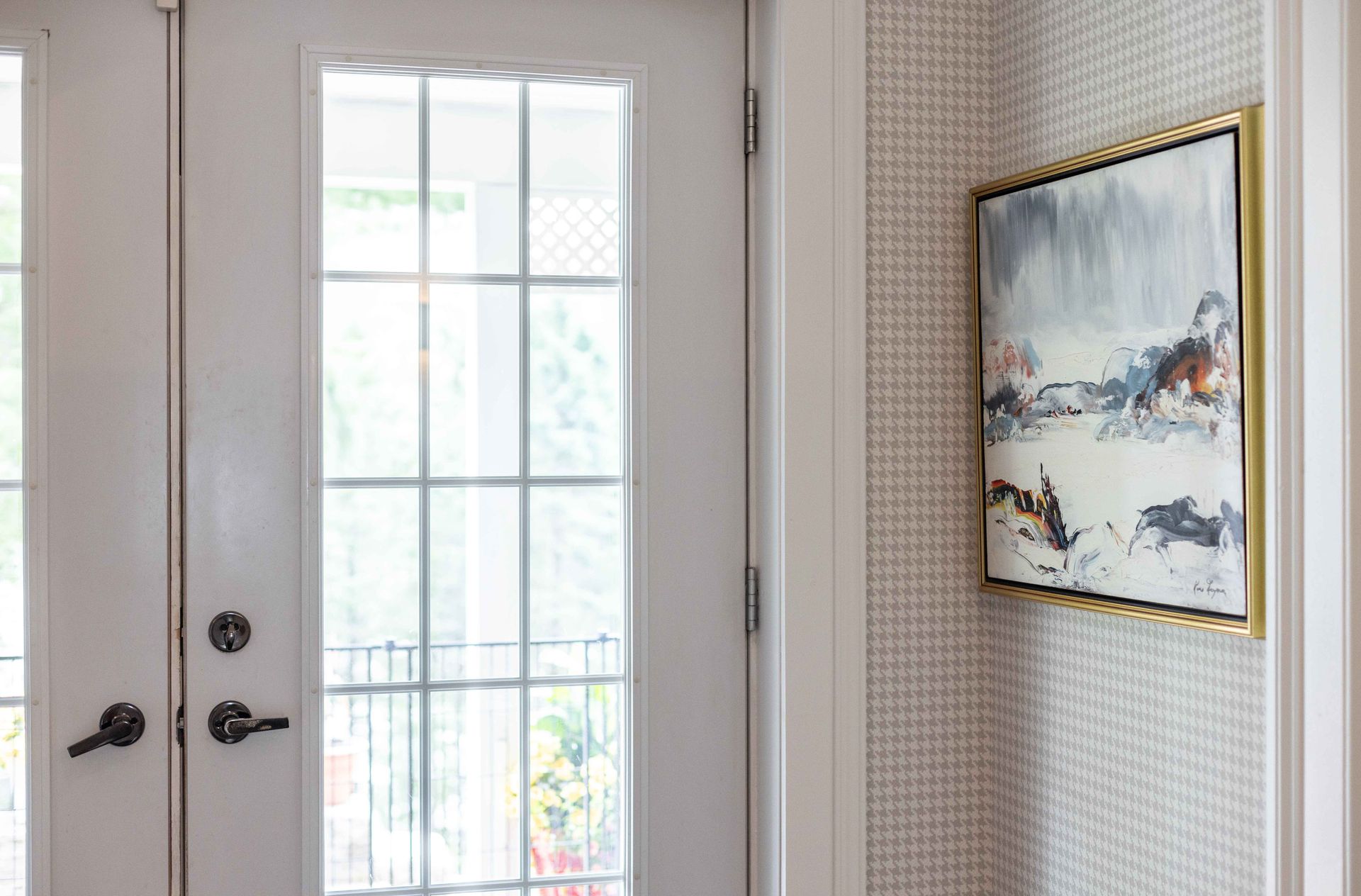 Porte blanche vitrée et tableau encadré sur un mur à motifs.
