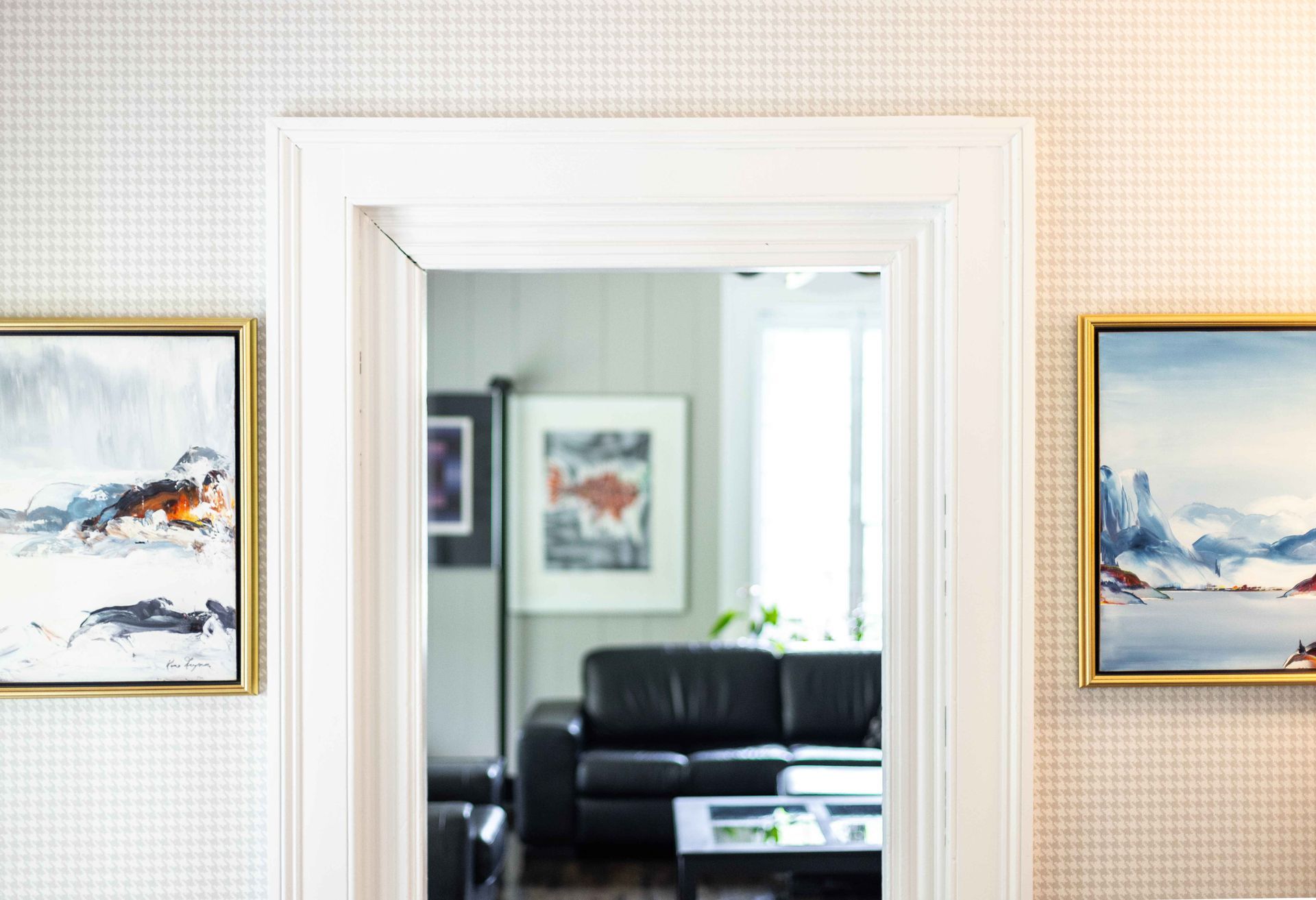 Porte blanche encadrée de deux tableaux, donnant sur un salon avec un canapé noir.