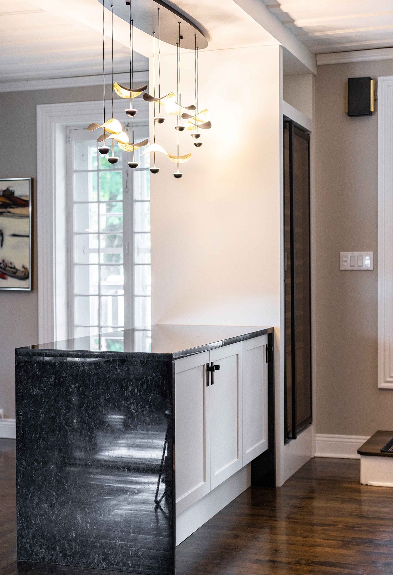 Îlot de cuisine avec comptoir en granit noir, armoires blanches et luminaire moderne.