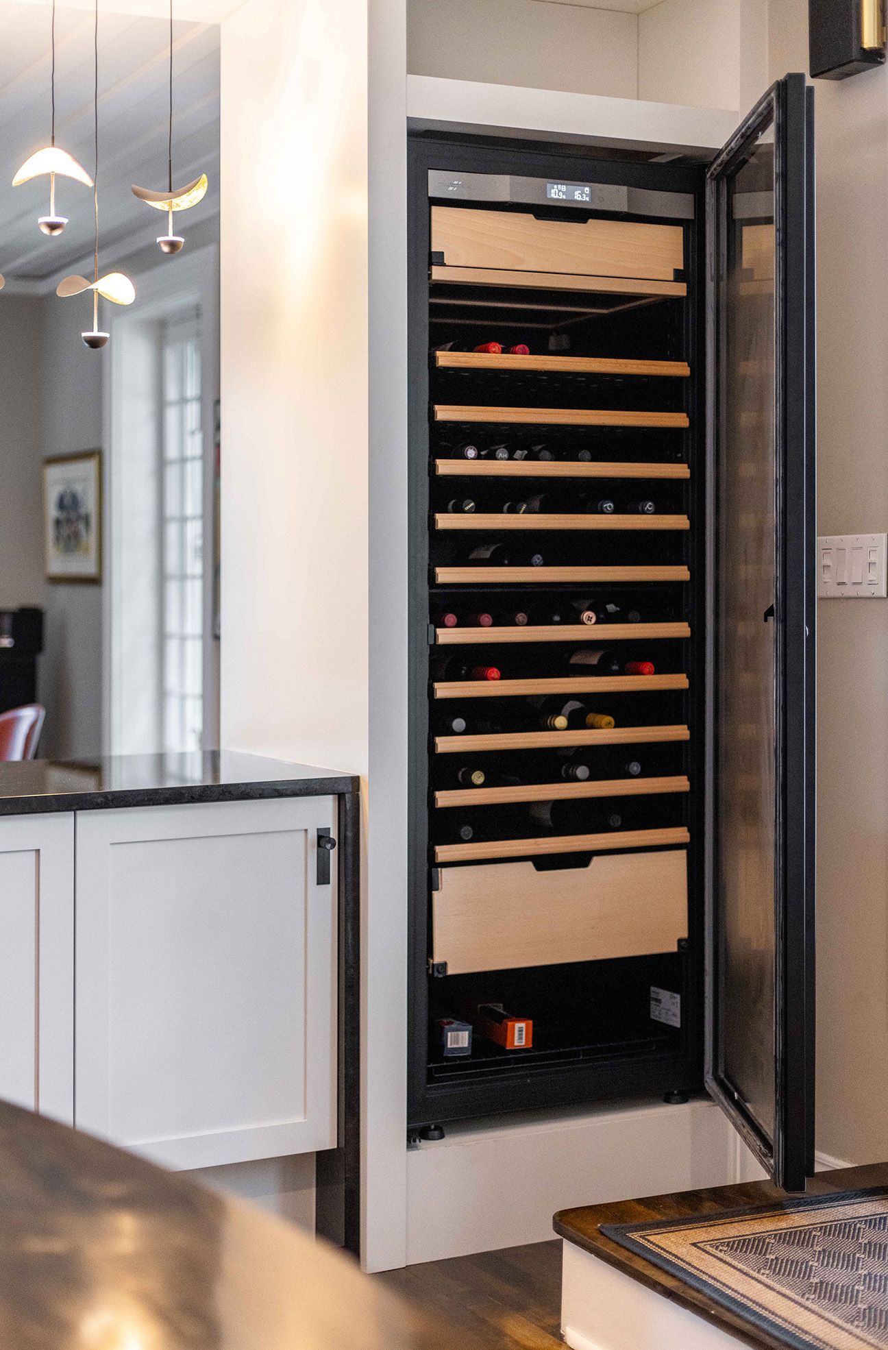 Une cave à vin encastrée avec une porte vitrée ouverte, dévoilant des rangées de bouteilles de vin et des étagères en bois.