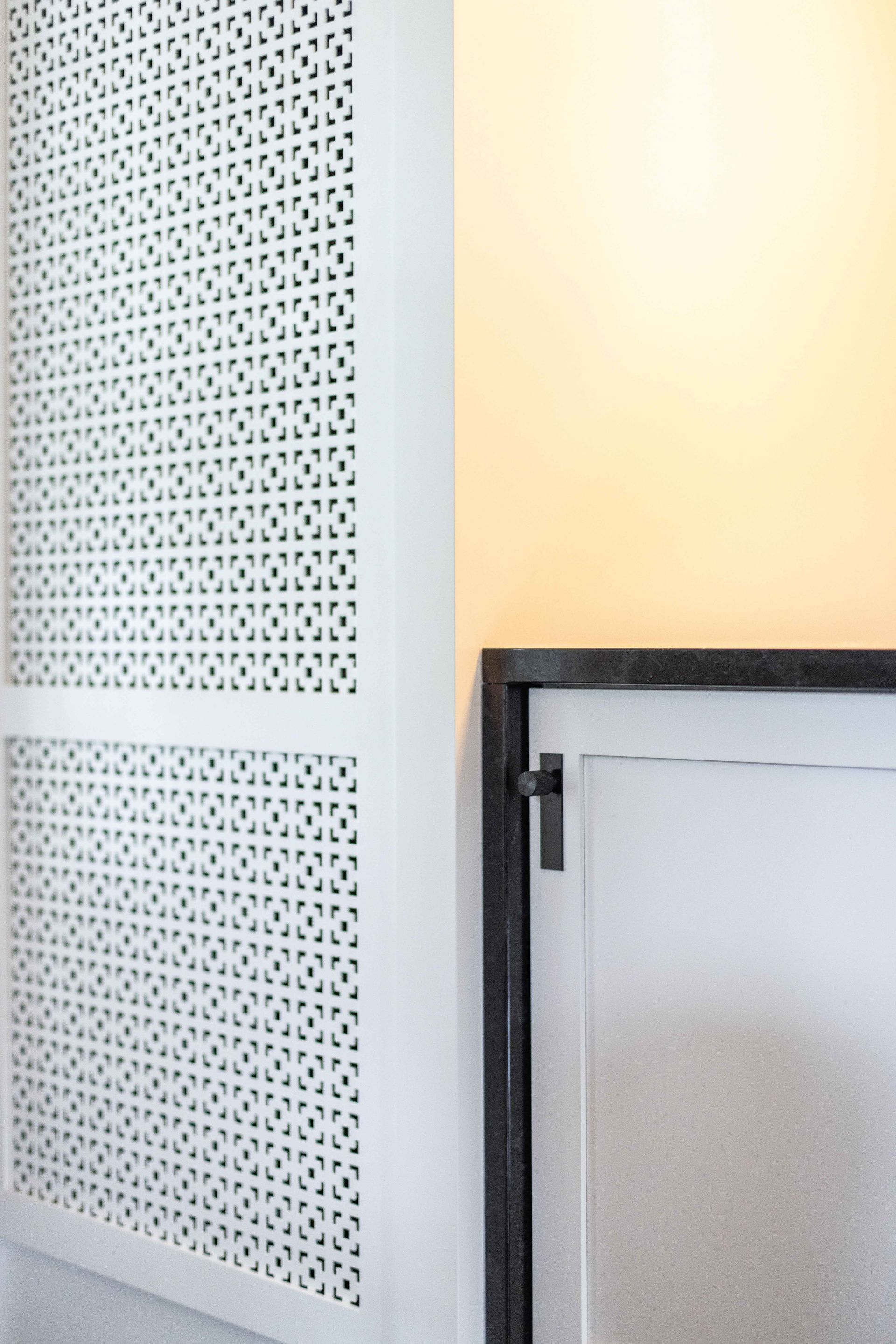 Panneau blanc perforé sur un mur orange clair et une porte blanche à cadre noir.