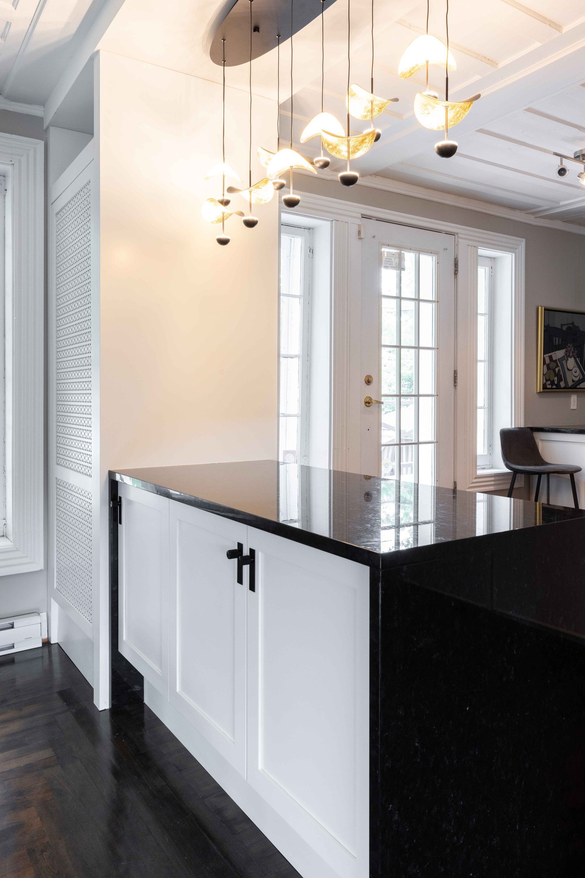 Îlot de cuisine noir et blanc avec un plan de travail foncé et des placards blancs. Éclairage décoratif au-dessus.