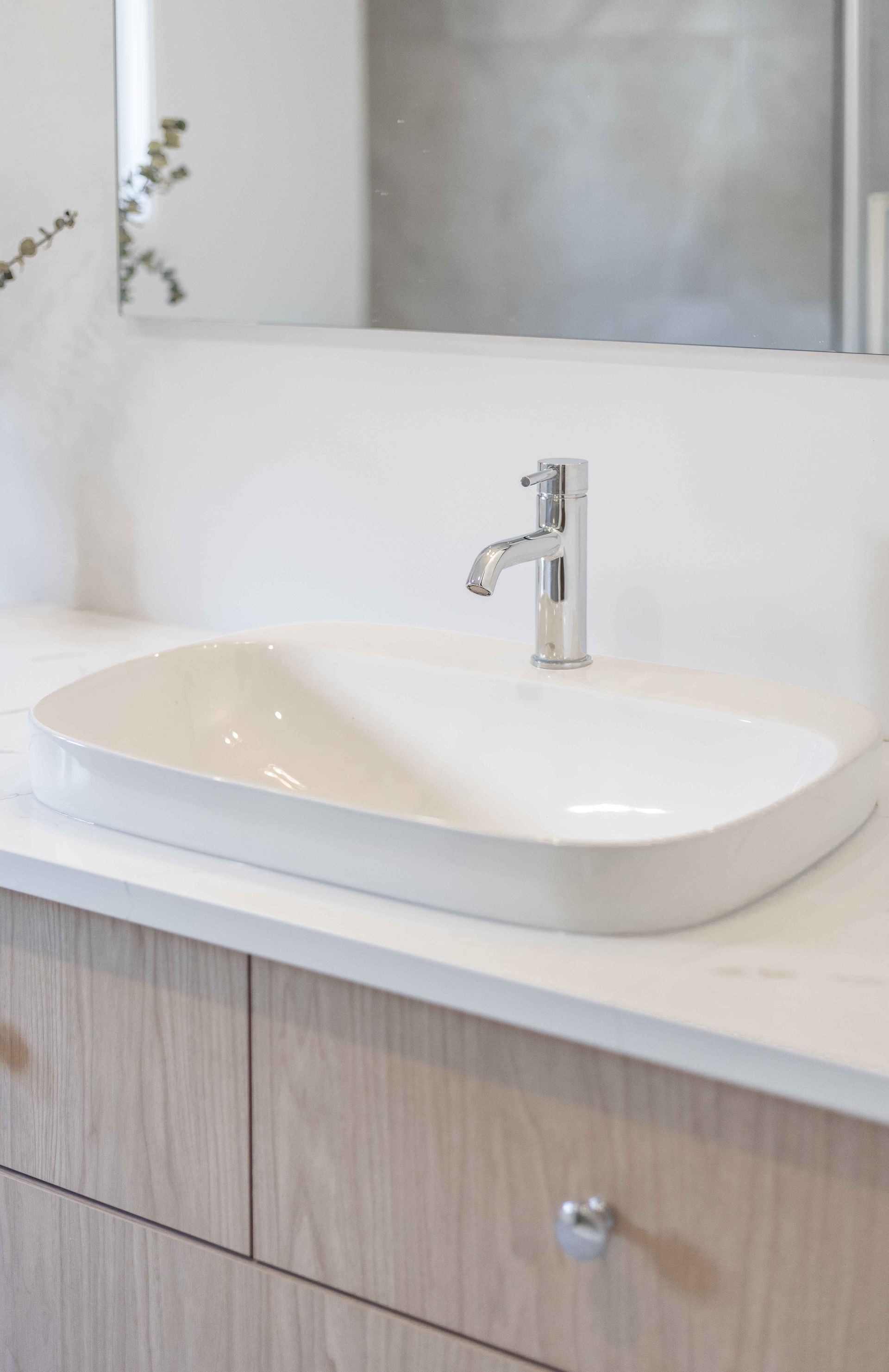 Lavabo ovale blanc sur un plan de travail clair avec robinet chromé, meubles en bois clair en dessous.