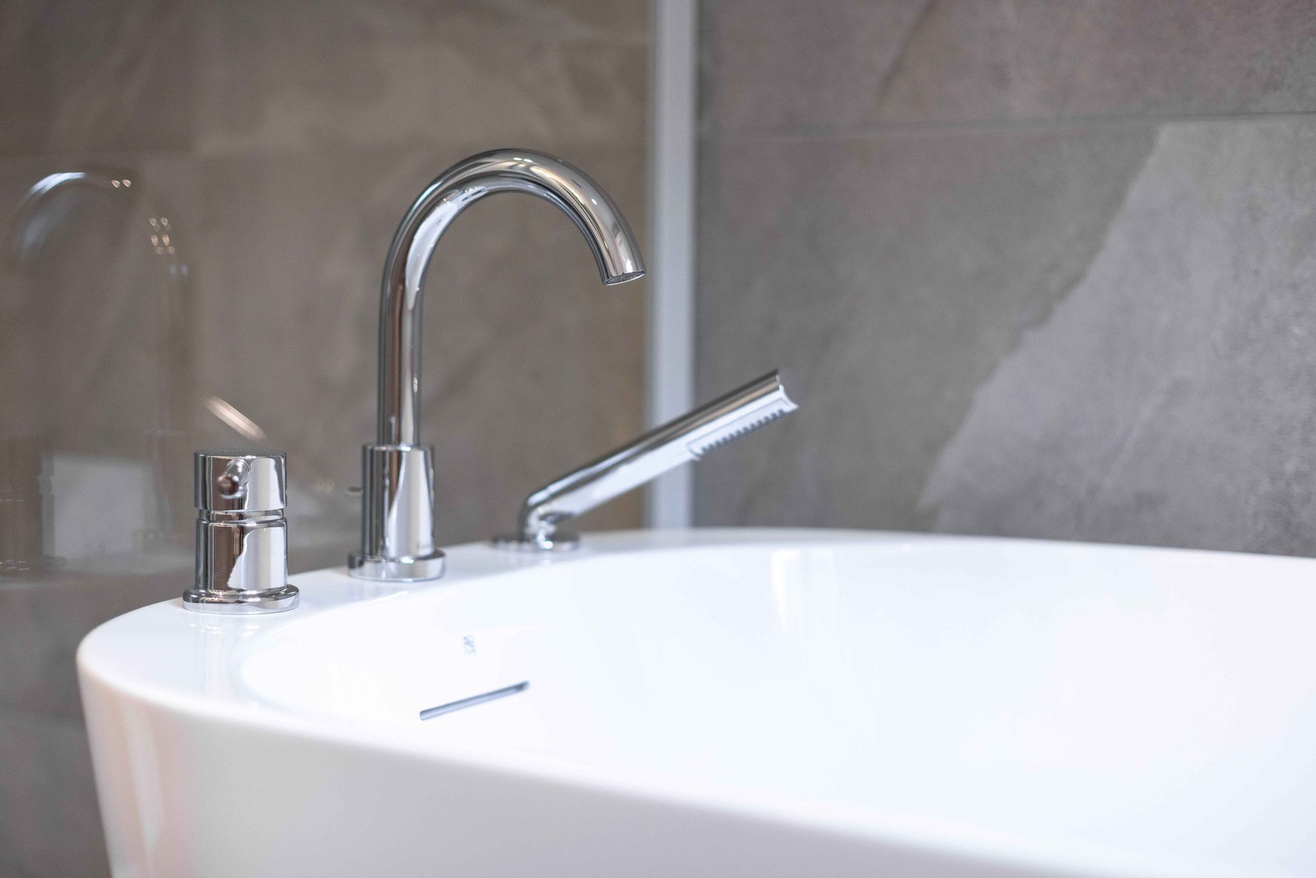 Gros plan sur une baignoire blanche avec robinetterie argentée, devant un mur carrelé gris.