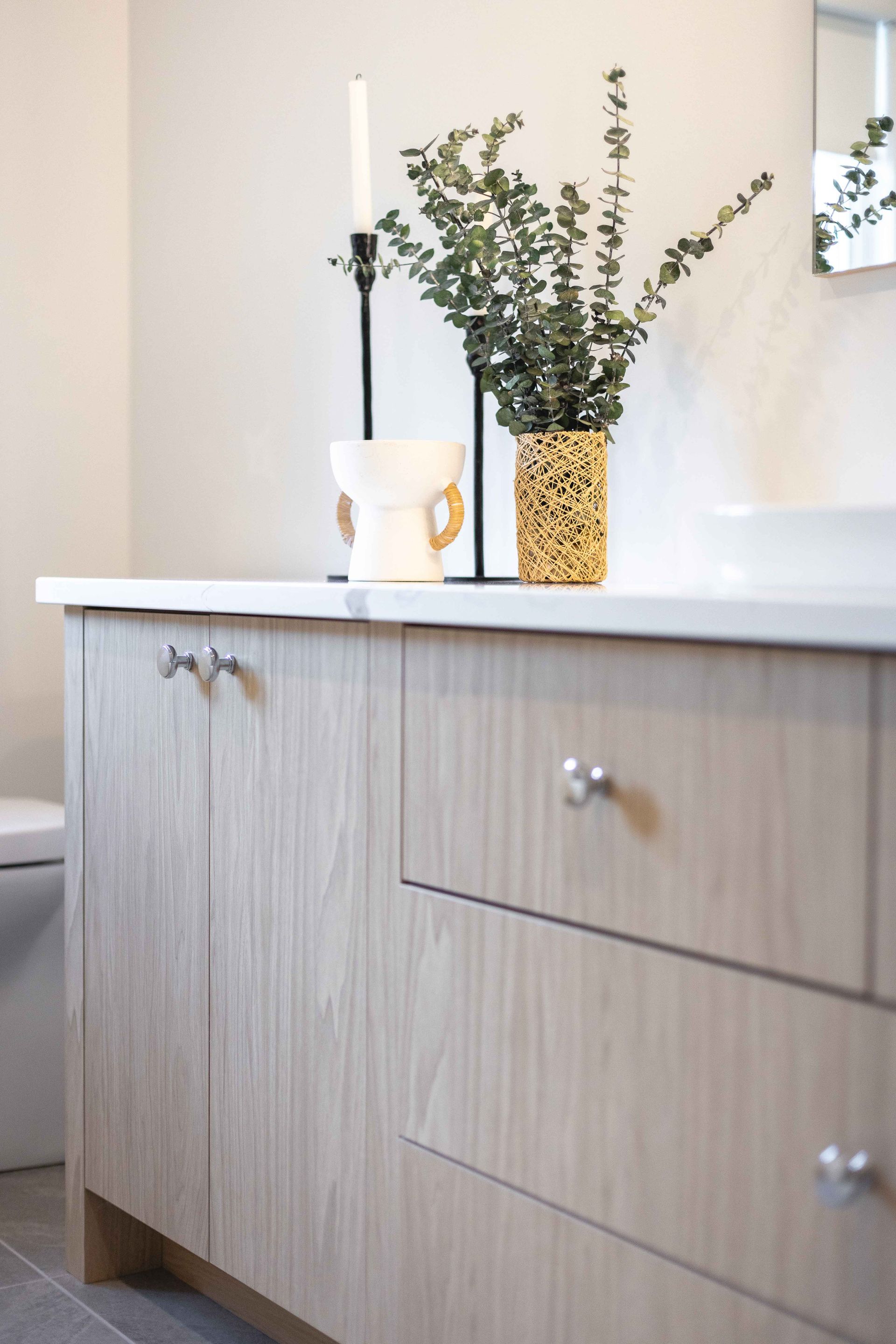 Meuble-lavabo de salle de bain avec armoires en bois clair, comptoir blanc et plantes décoratives.