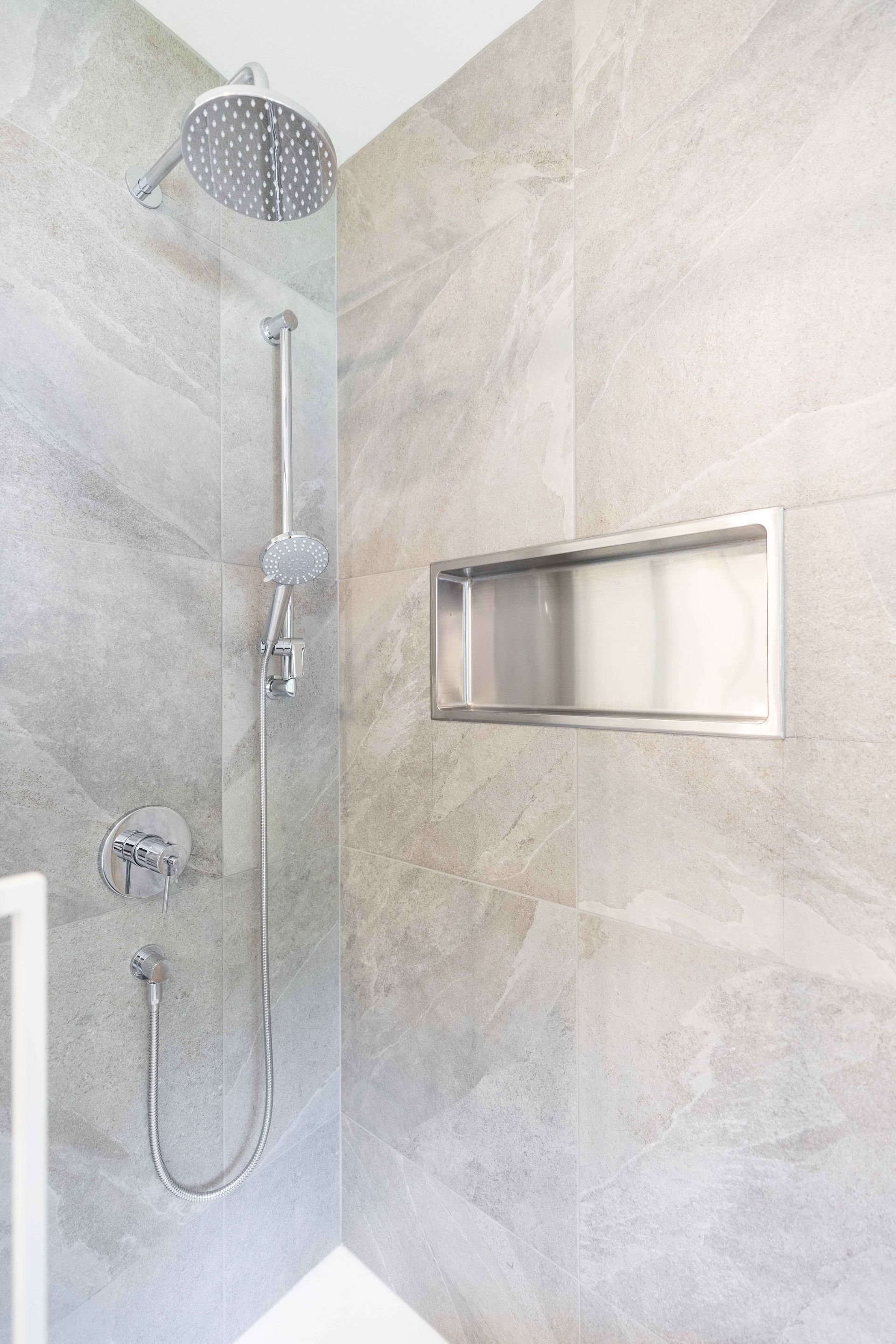 Douche avec carrelage gris, robinetterie argentée et étagère encastrée.