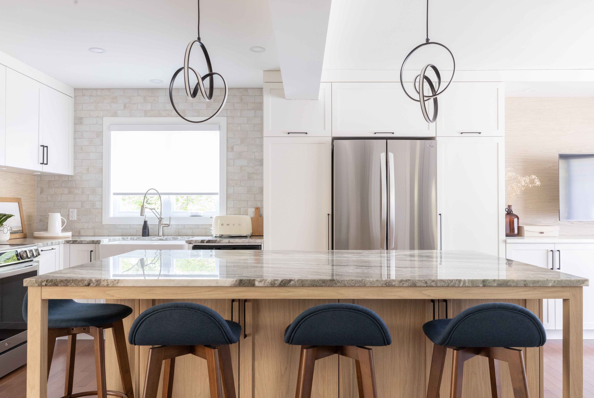 Cuisine moderne avec îlot central, armoires blanches, appareils électroménagers en acier inoxydable et luminaires suspendus.