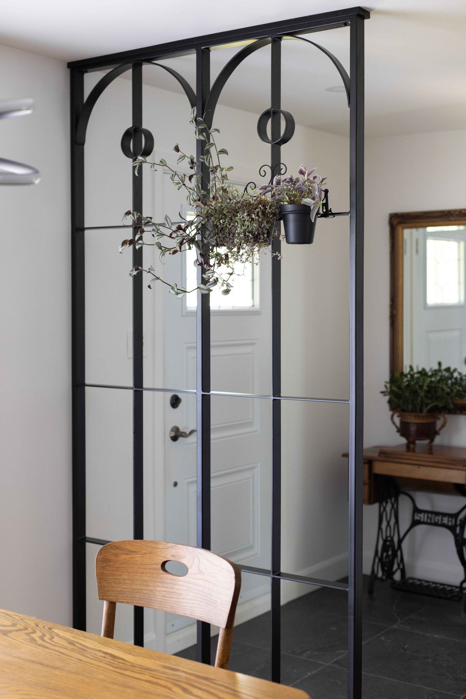 Paravent en métal noir et verre avec plante suspendue, séparant la salle à manger de l'entrée.