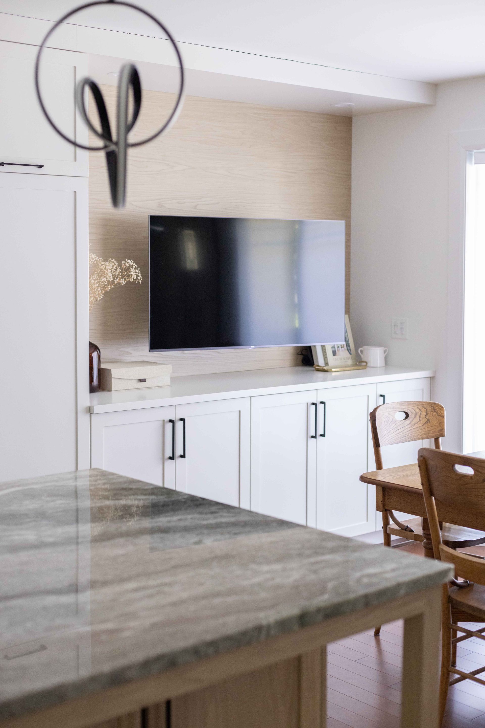 Cuisine avec placards, télévision et plan de travail en marbre. Une chaise en bois et des ciseaux décoratifs sont visibles.