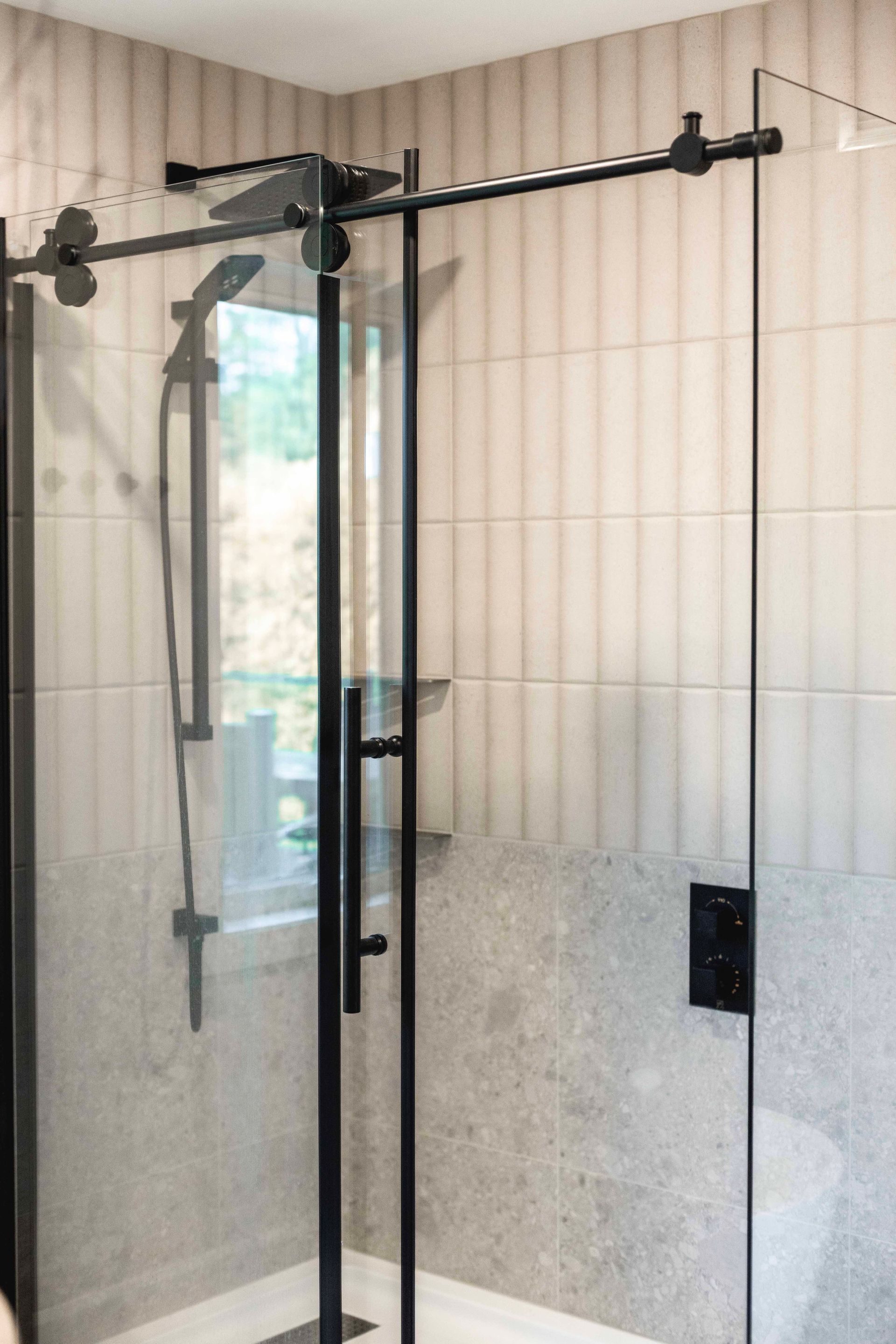 Douche moderne avec paroi de douche en verre à cadre noir, pommeau de douche et murs carrelés.