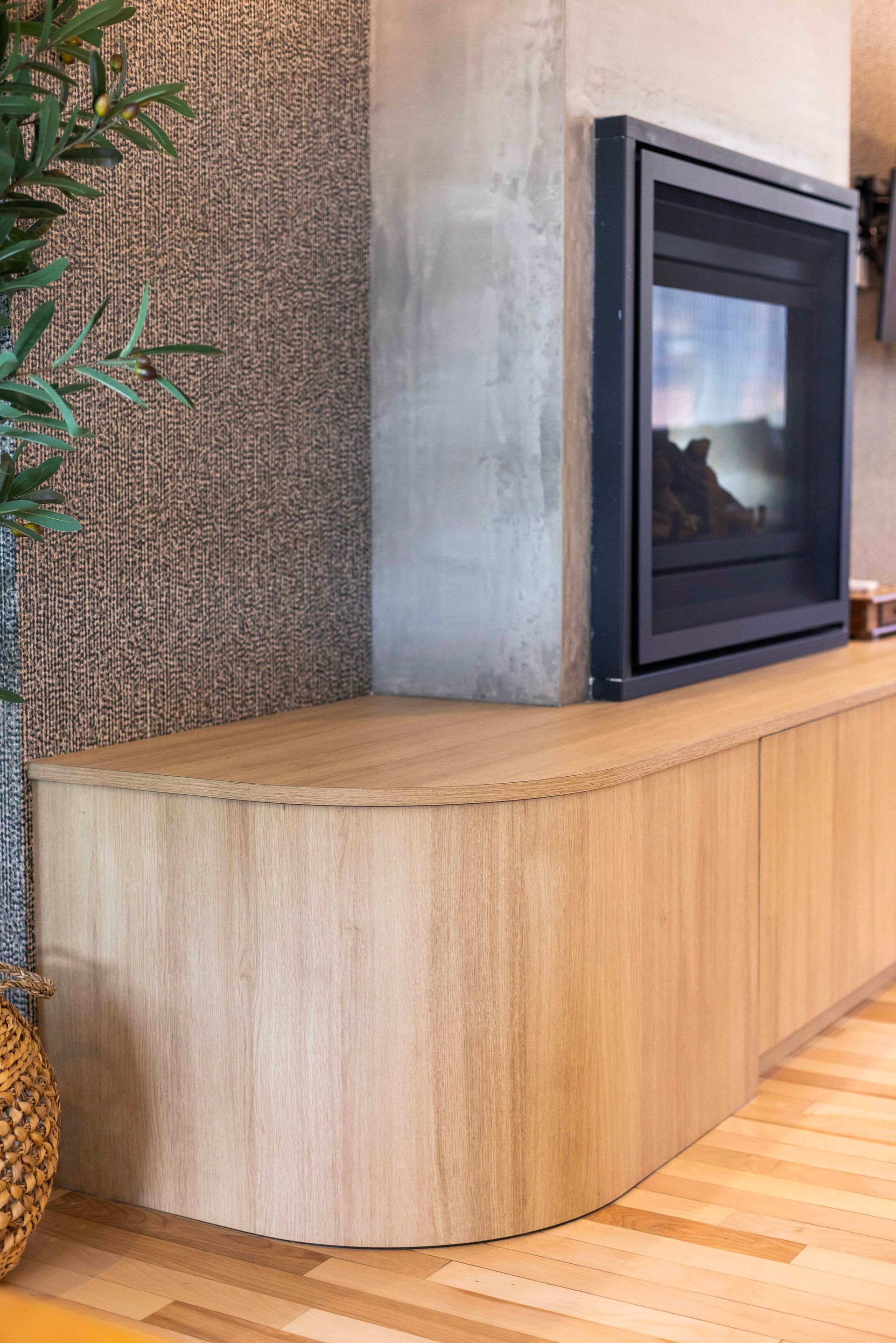 Meuble en bois à façade incurvée, cheminée et mur texturé dans un salon.