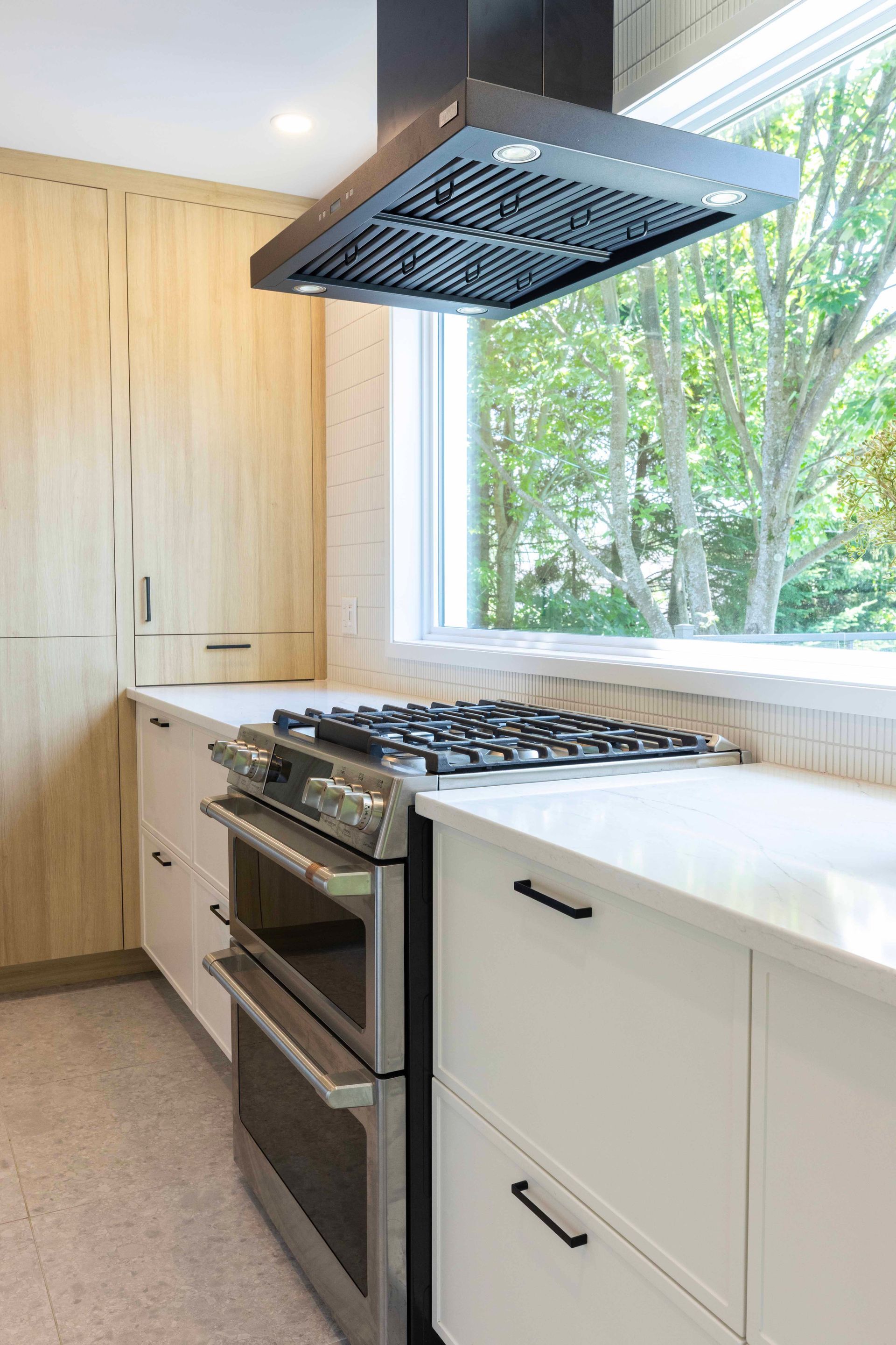 Cuisine moderne avec four et plaque de cuisson en acier inoxydable, placards blancs et grande fenêtre.