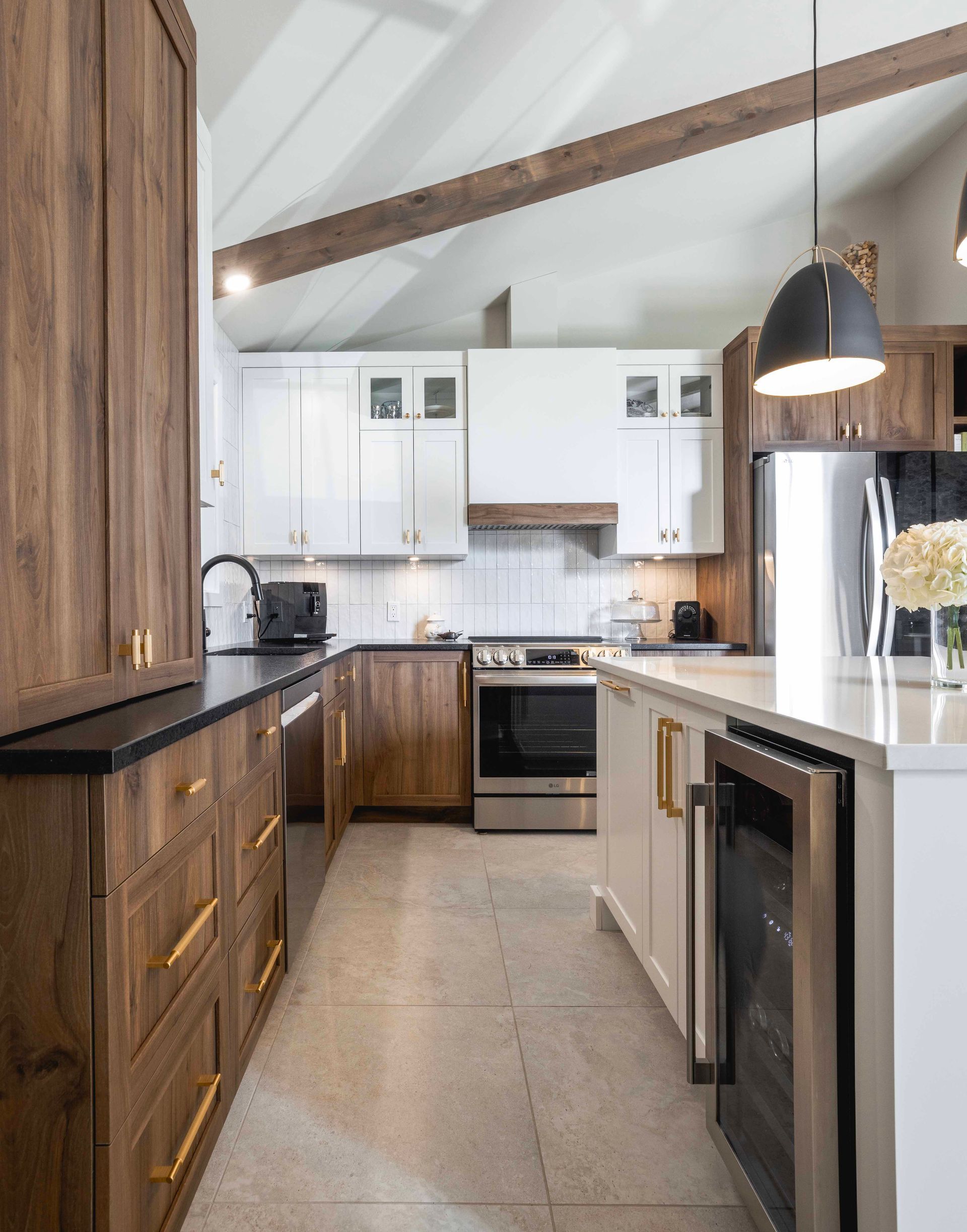 Cuisine moderne avec armoires en bois et blanches, électroménagers en acier inoxydable et îlot central.