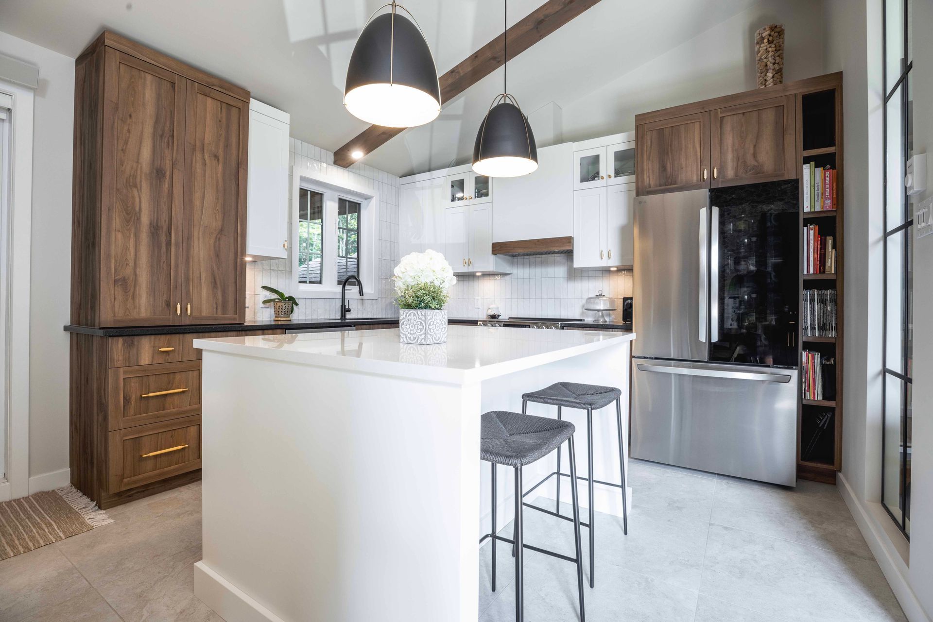 Cuisine moderne avec îlot central blanc, appareils électroménagers en acier inoxydable, armoires en bois foncé et deux suspensions lumineuses.