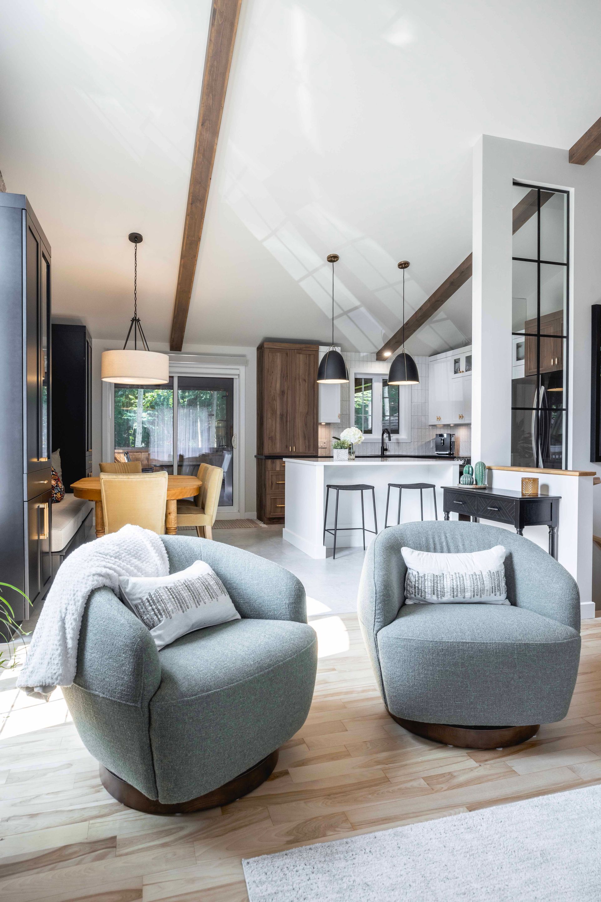 Deux fauteuils pivotants bleu sarcelle dans un salon moderne et lumineux, avec poutres apparentes et vue sur la cuisine.