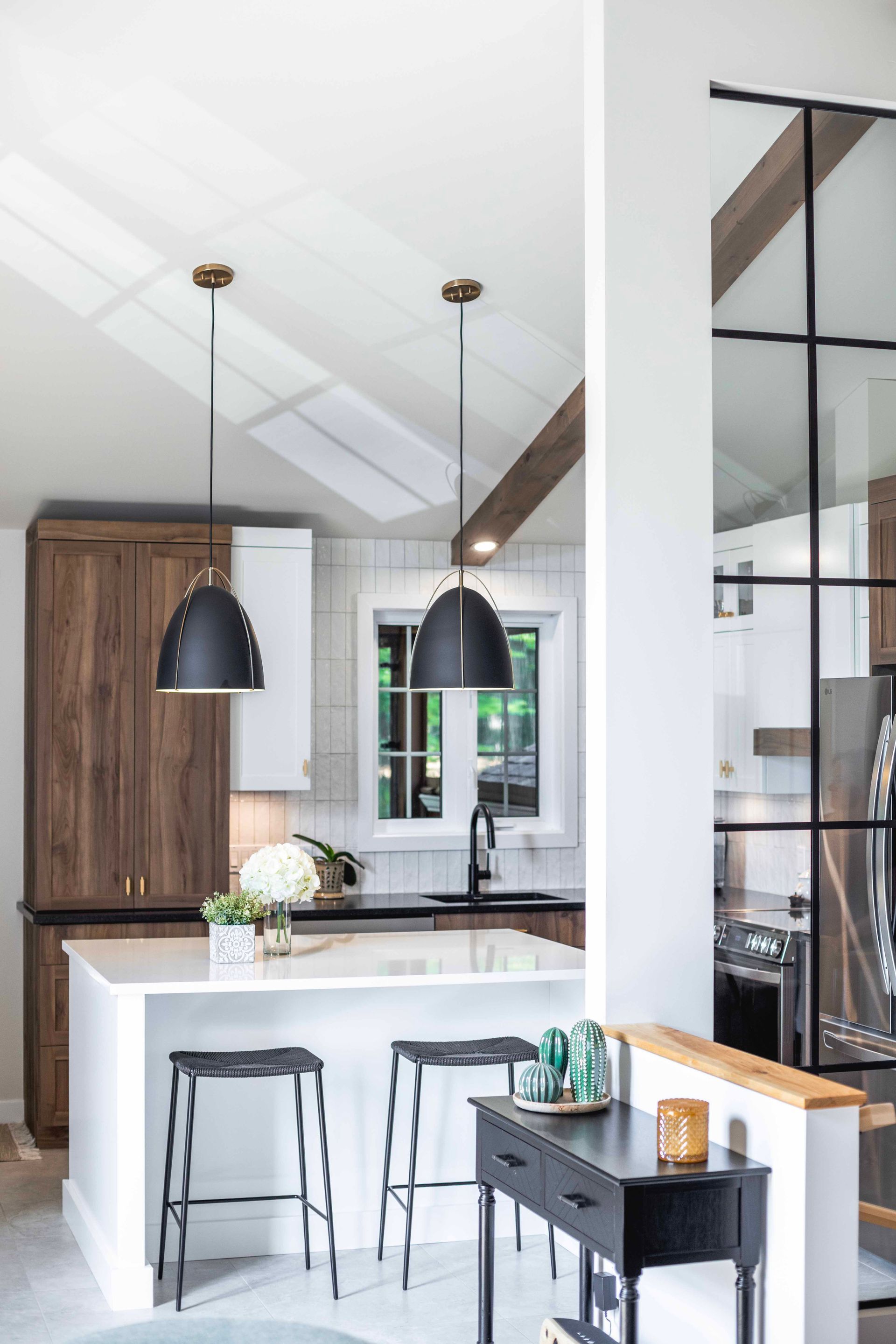 Cuisine moderne avec îlot central, suspensions lumineuses foncées, plan de travail blanc et placards en bois foncé.