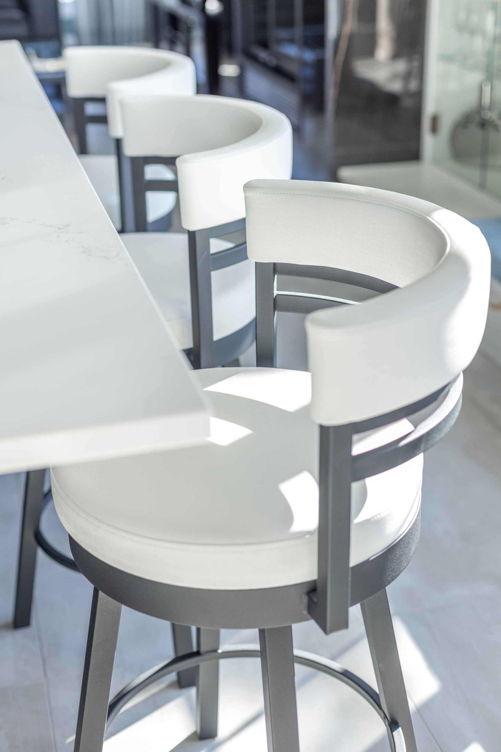 Tabourets de bar blancs rembourrés devant un comptoir blanc, avec une structure en métal gris.