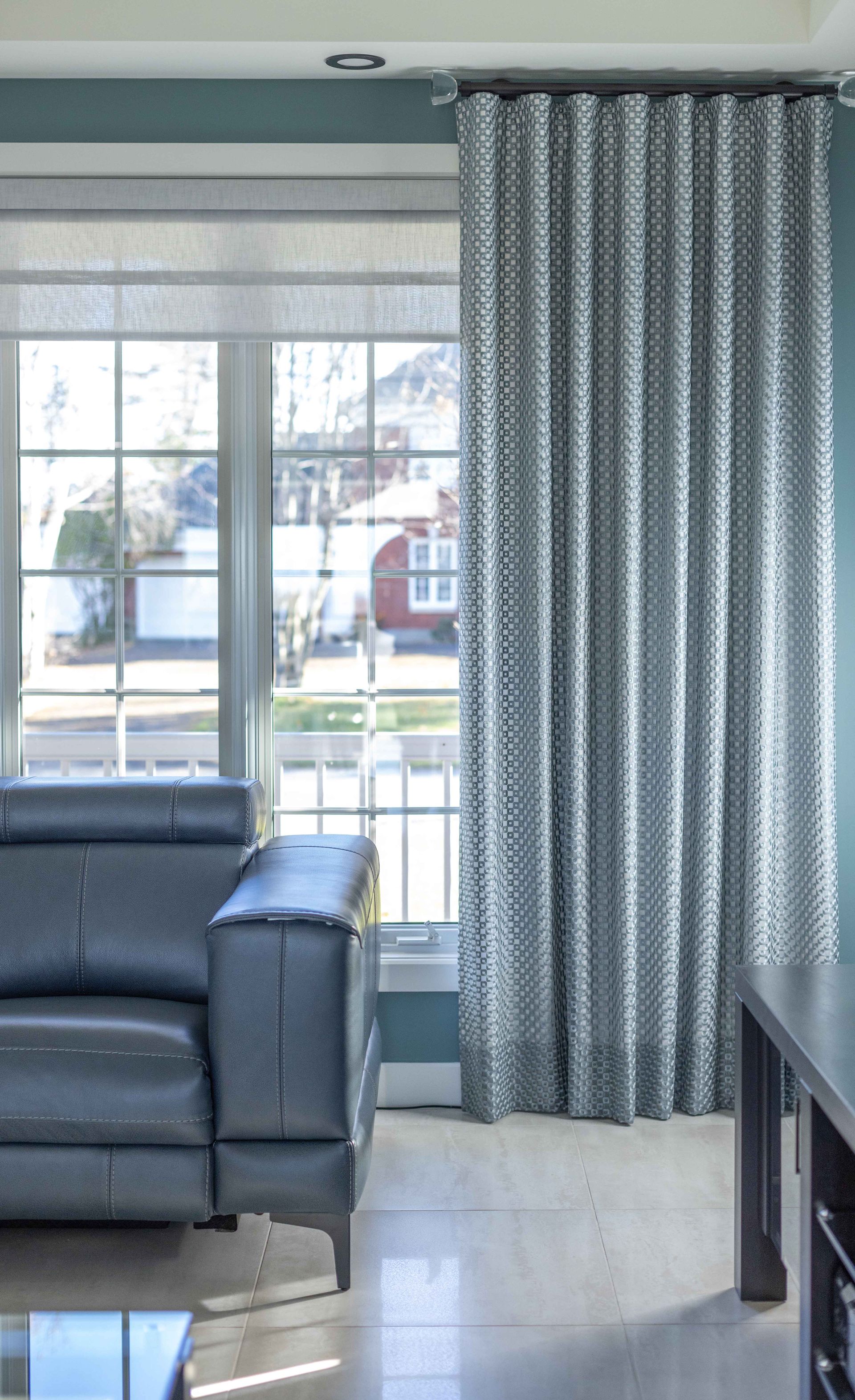 Salon avec canapé bleu, rideaux à motifs et fenêtre donnant sur une rue.