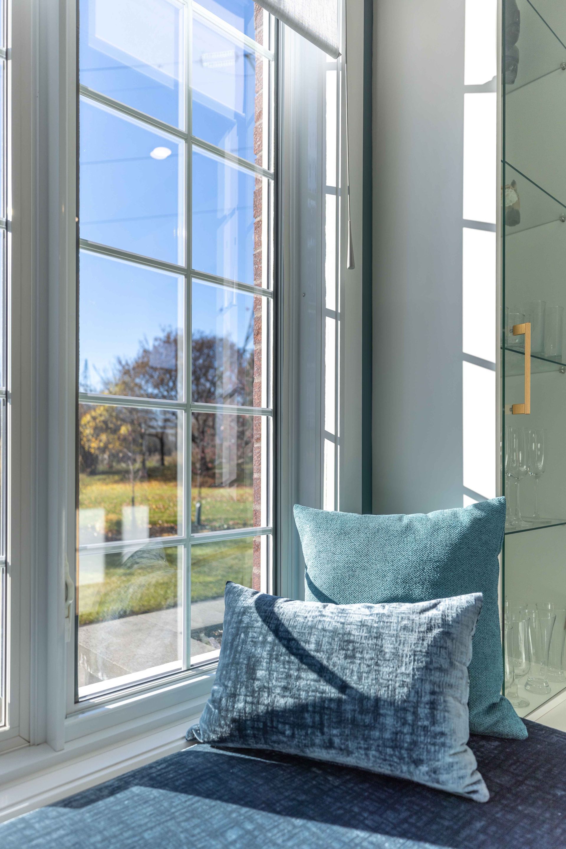Banquette près de la fenêtre avec coussins turquoise donnant sur une cour ensoleillée, avec une porte vitrée en arrière-plan.