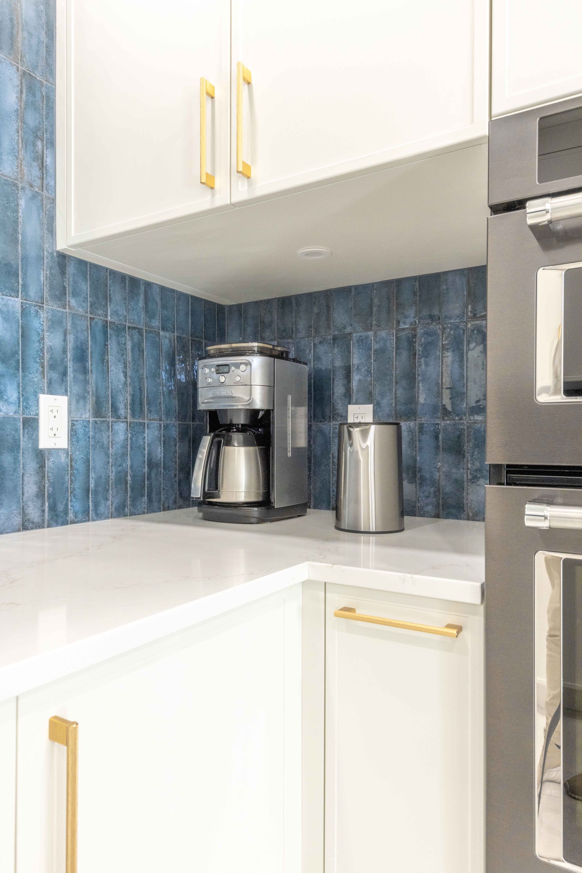Coin cuisine blanc avec crédence carrelée bleue, cafetière et robinetterie dorée.