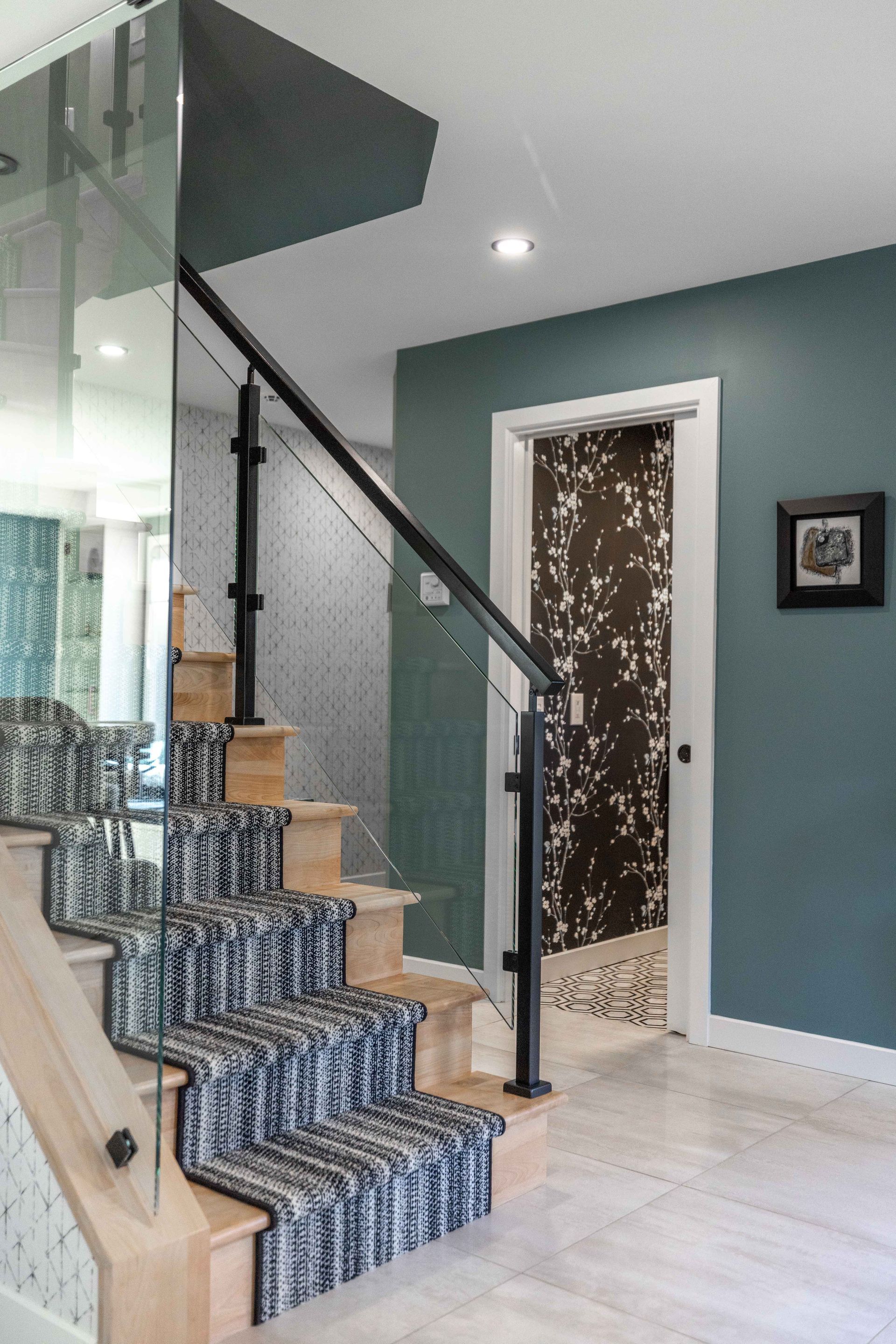 Escalier avec marches en bois clair, tapis de couloir à motifs, rampe noire et murs turquoise.