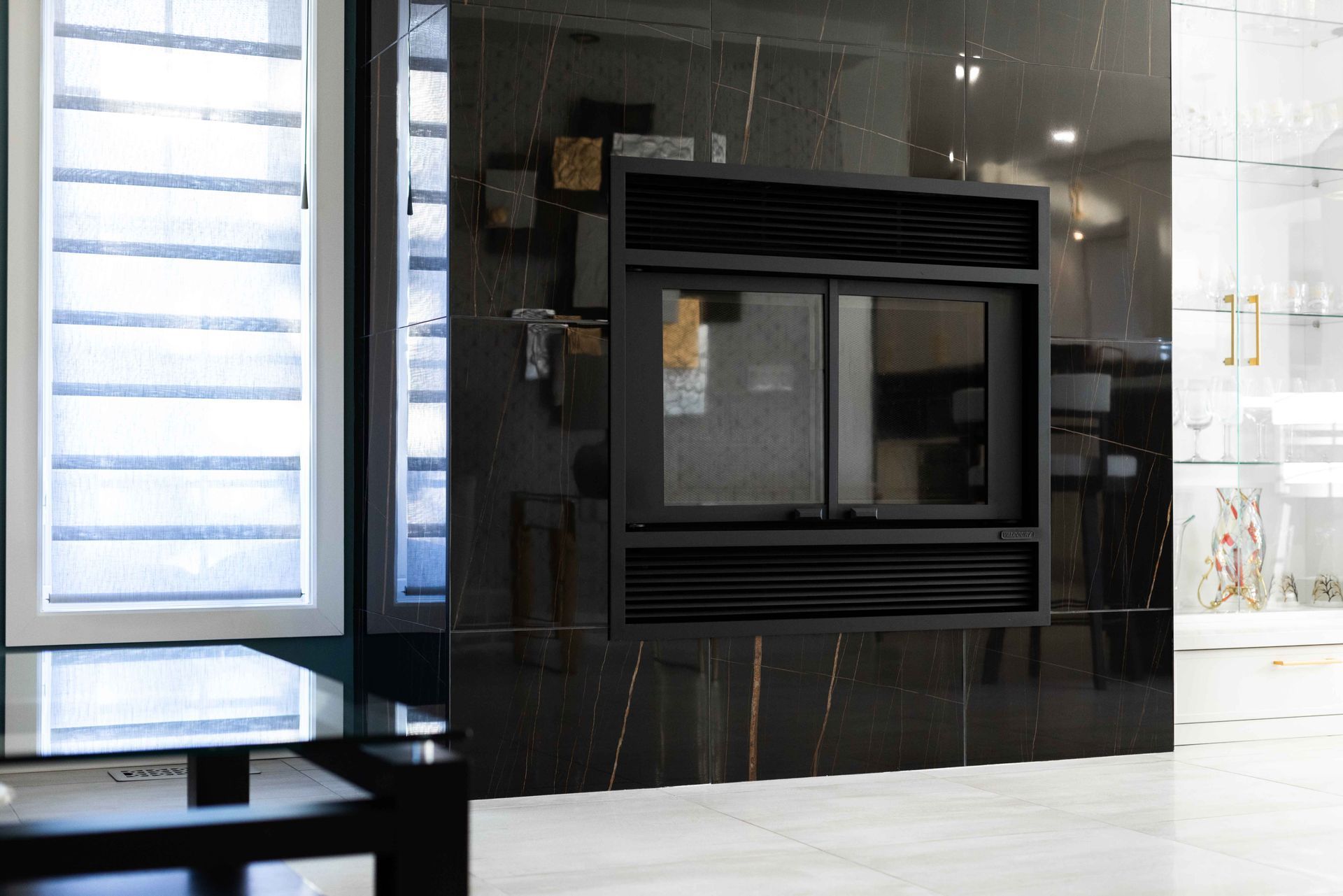 Cheminée noire aux détails ondulés, adossée à un mur de marbre foncé dans une pièce moderne.