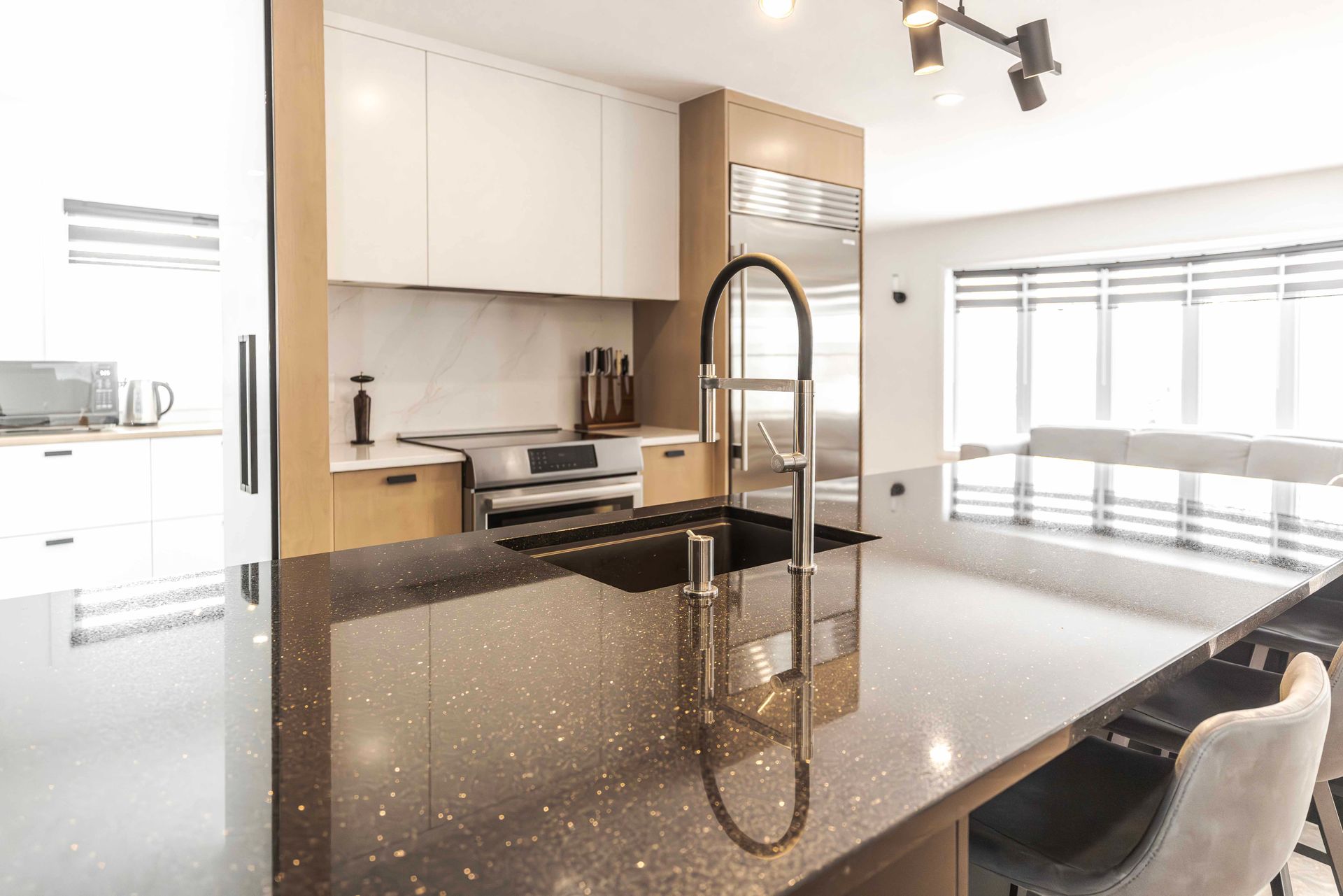 Cuisine moderne avec îlot central en plan de travail noir, armoires blanches, électroménagers en acier inoxydable et coin bar.