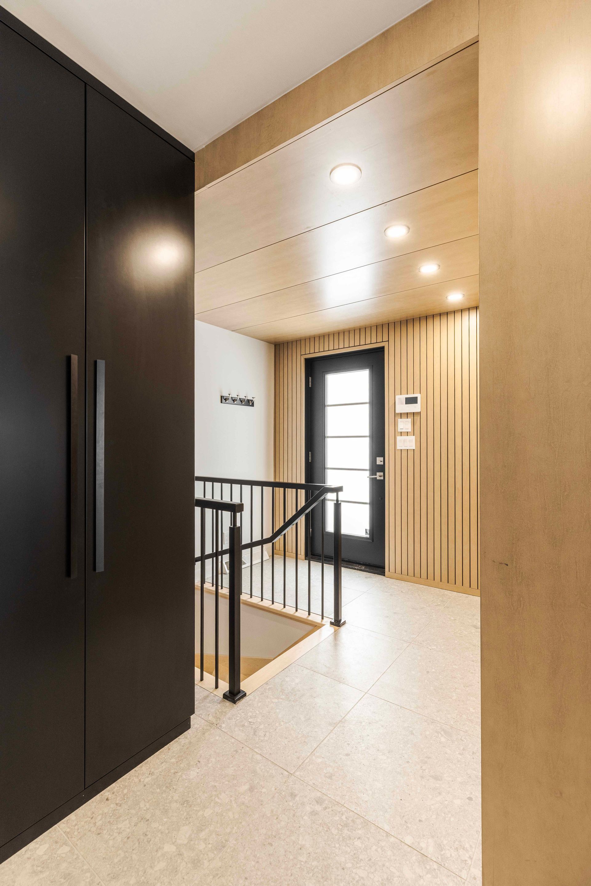 Couloir avec portes de placard sombres, murs texturés et une porte au fond.
