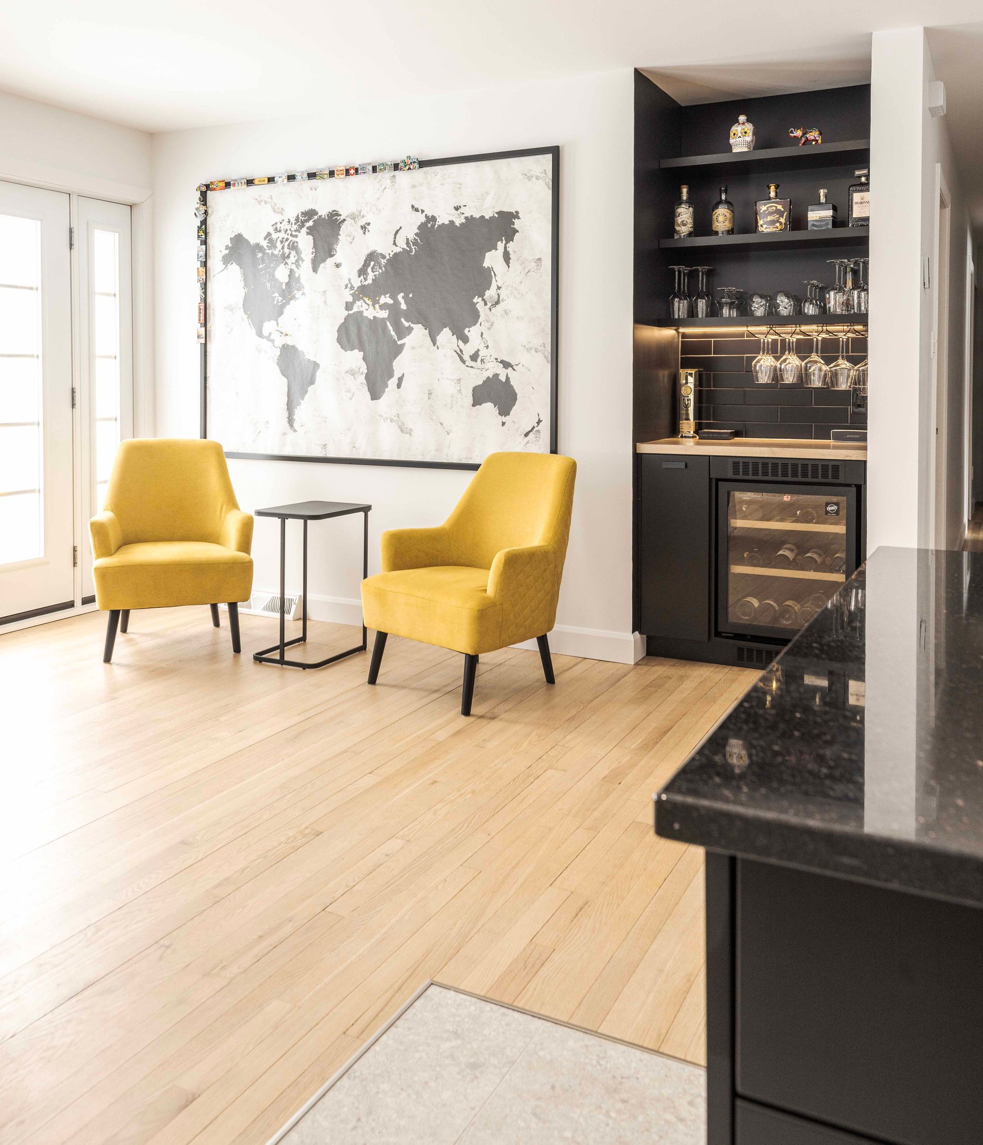 Salon avec fauteuils jaunes, carte du monde et bar noir avec cave à vin.