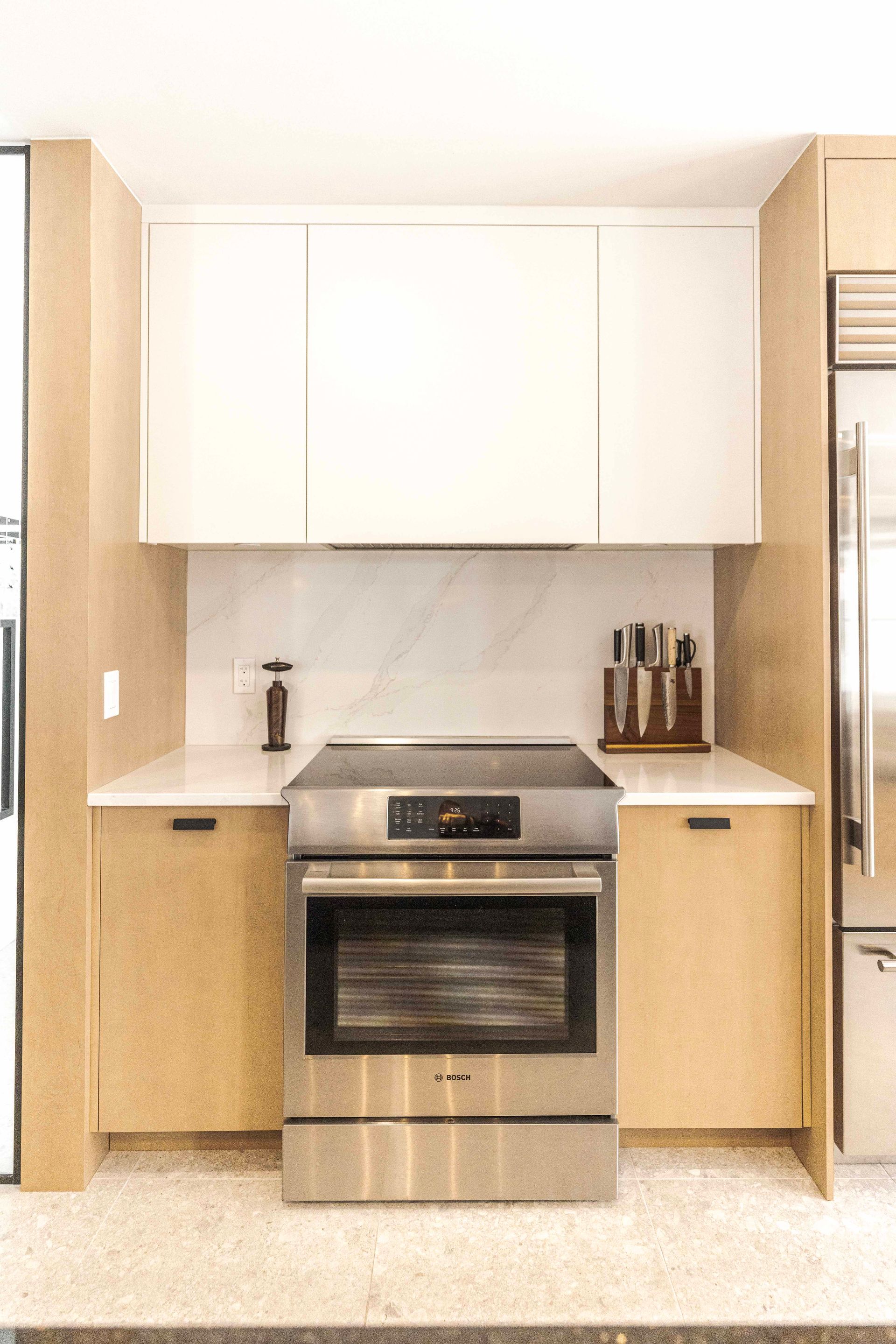Cuisine moderne avec four en acier inoxydable, armoires blanches et en bois, crédence en marbre.