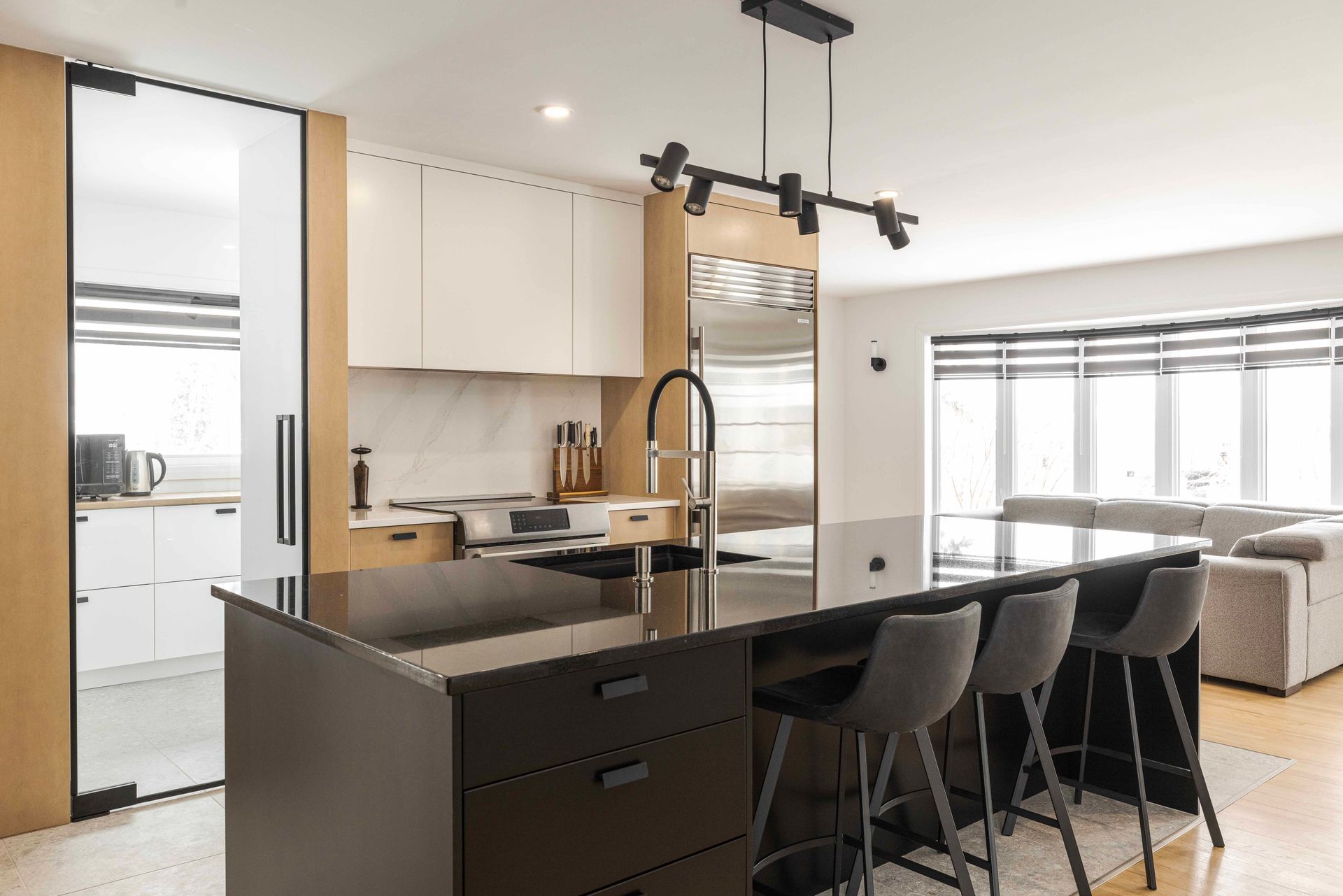 Cuisine moderne avec îlot central noir, tabourets de bar et éclairage sur rail.