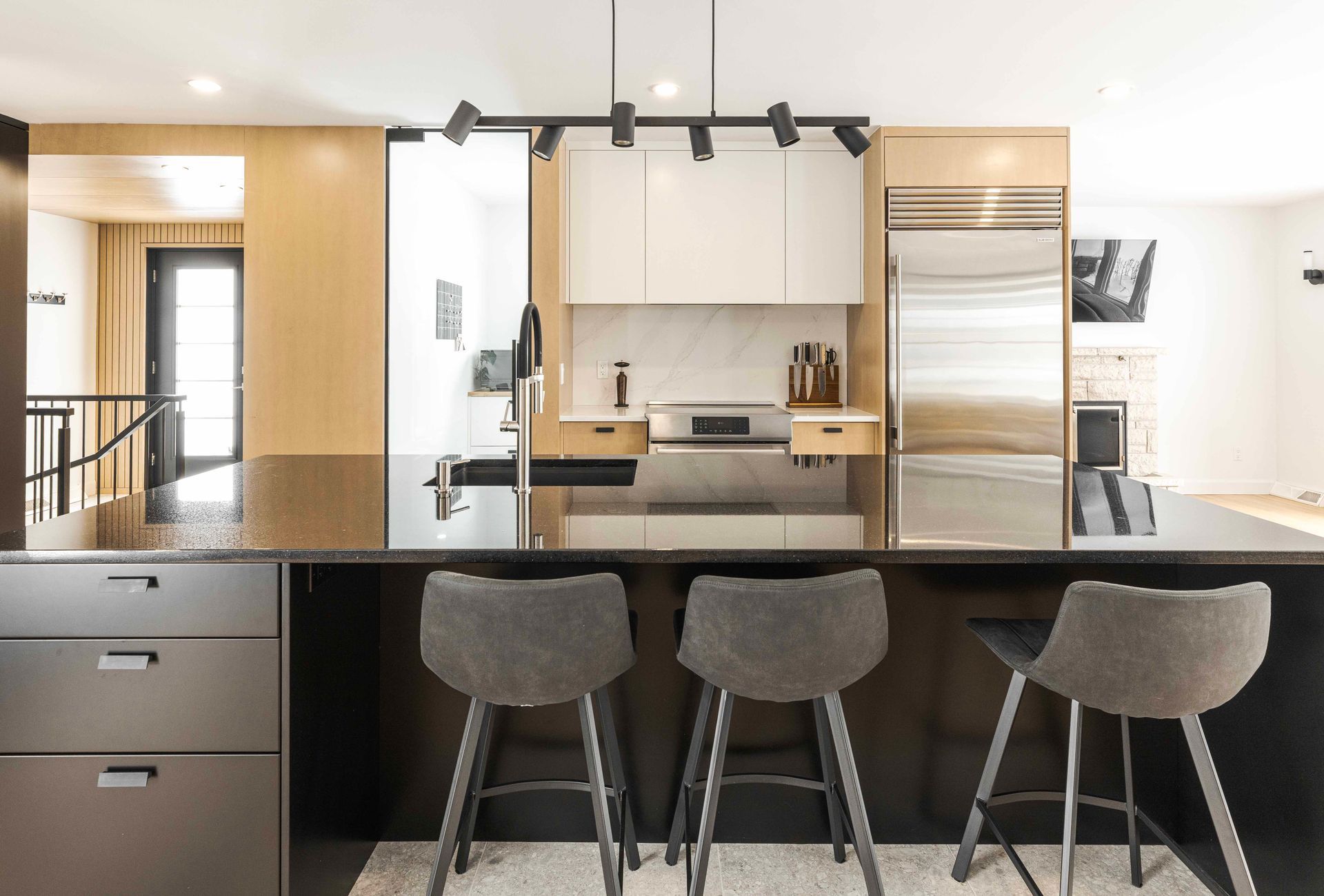 Cuisine moderne avec îlot central noir, placards blancs, réfrigérateur en acier inoxydable et tabourets de bar gris.