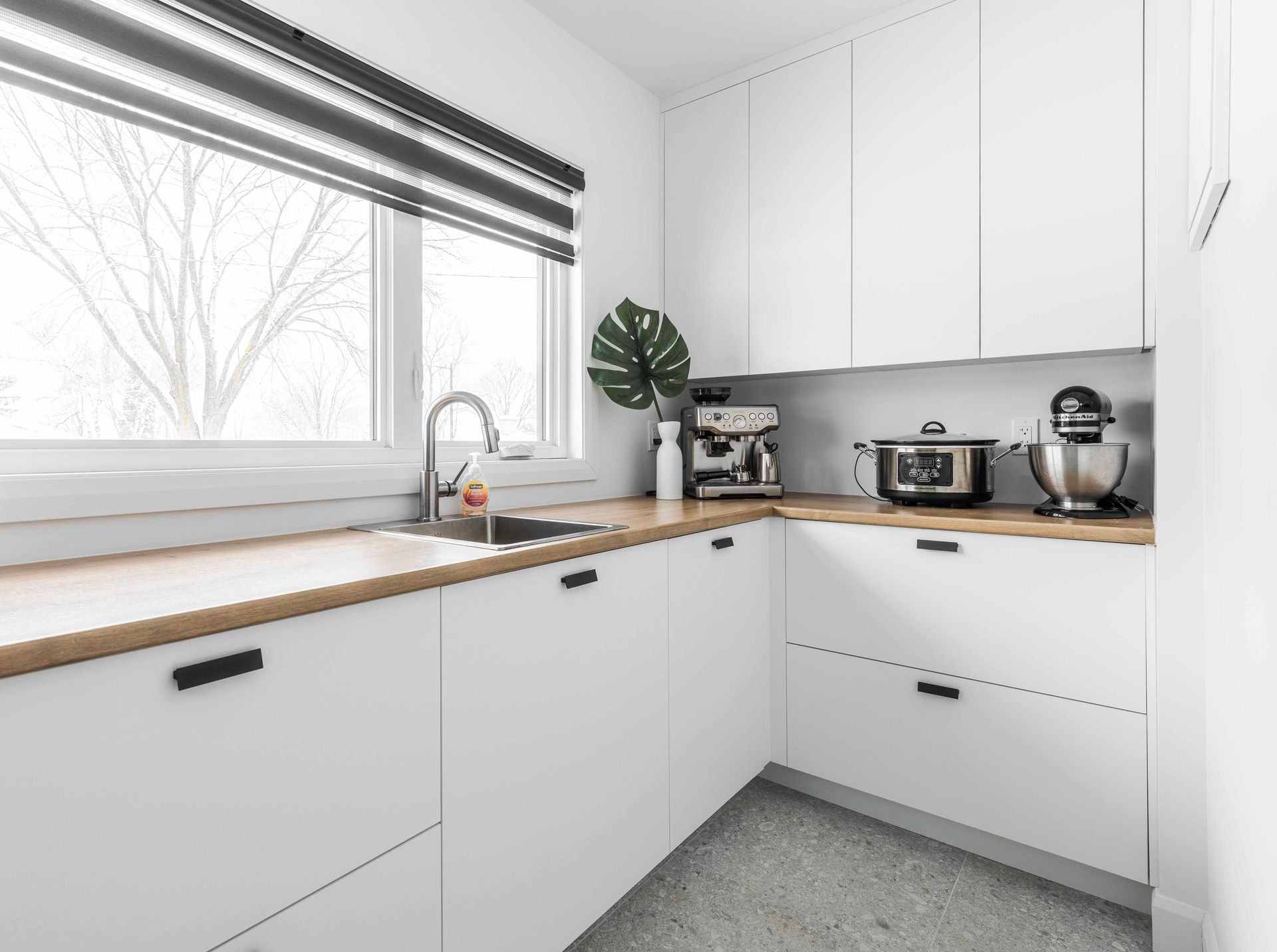 Cuisine moderne blanche avec comptoirs en bois clair, électroménagers en acier inoxydable et une fenêtre.