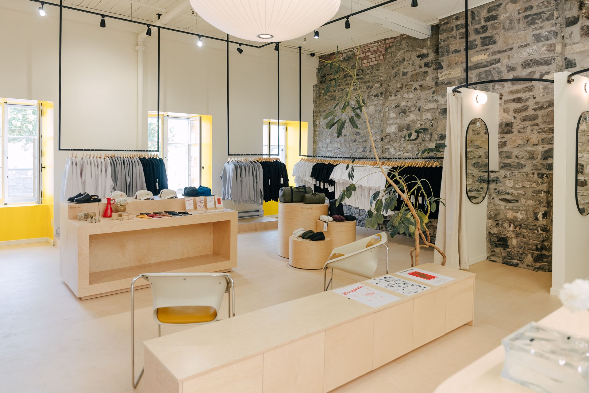 Intérieur d'un magasin de vêtements avec mur de briques apparentes, portants, présentoirs en bois et touches de jaune.