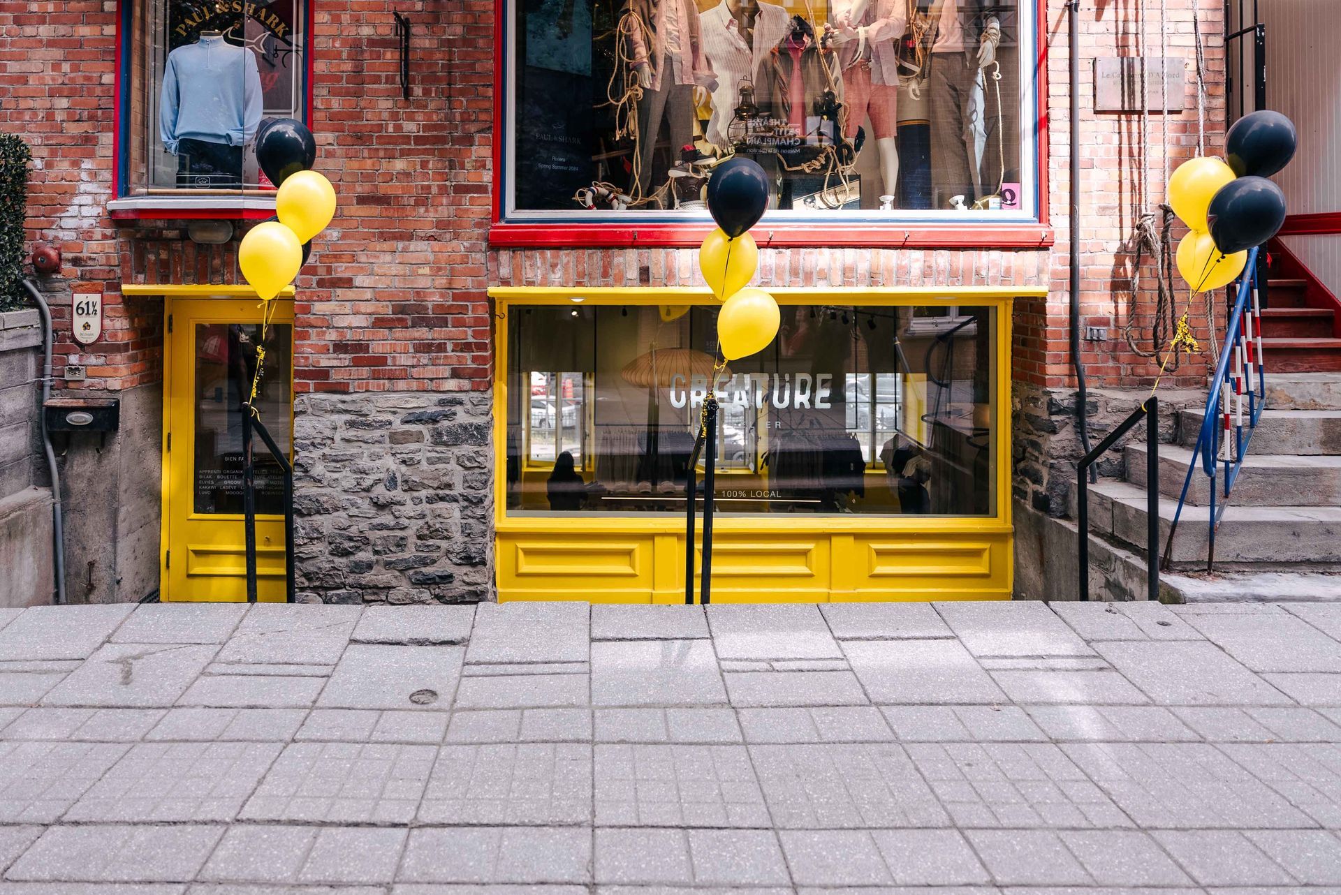 Façade jaune ornée de ballons, façade en briques rouges et rue pavée.
